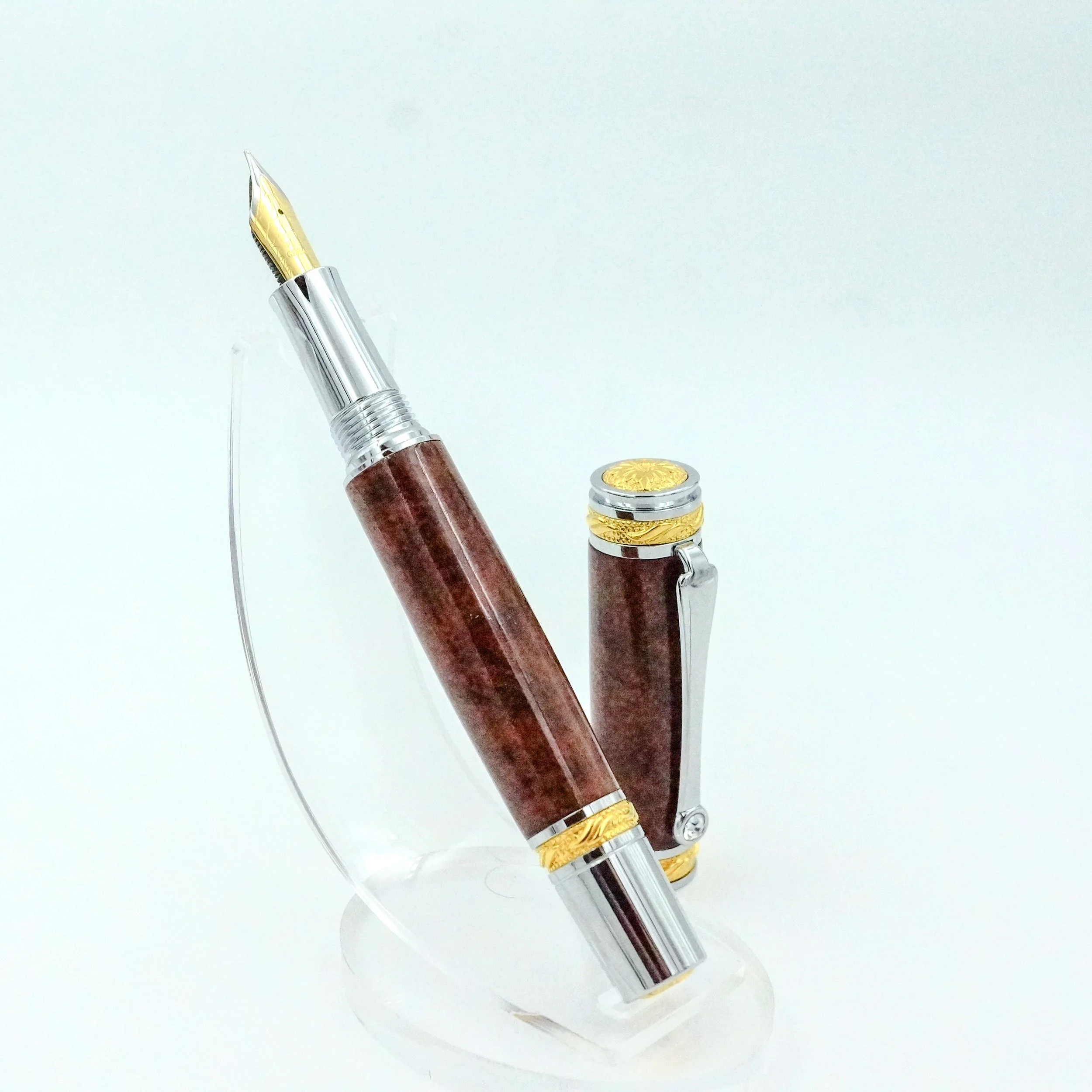 A luxury fountain pen with gold accents and a matching clip, resting on a clear display stand.
