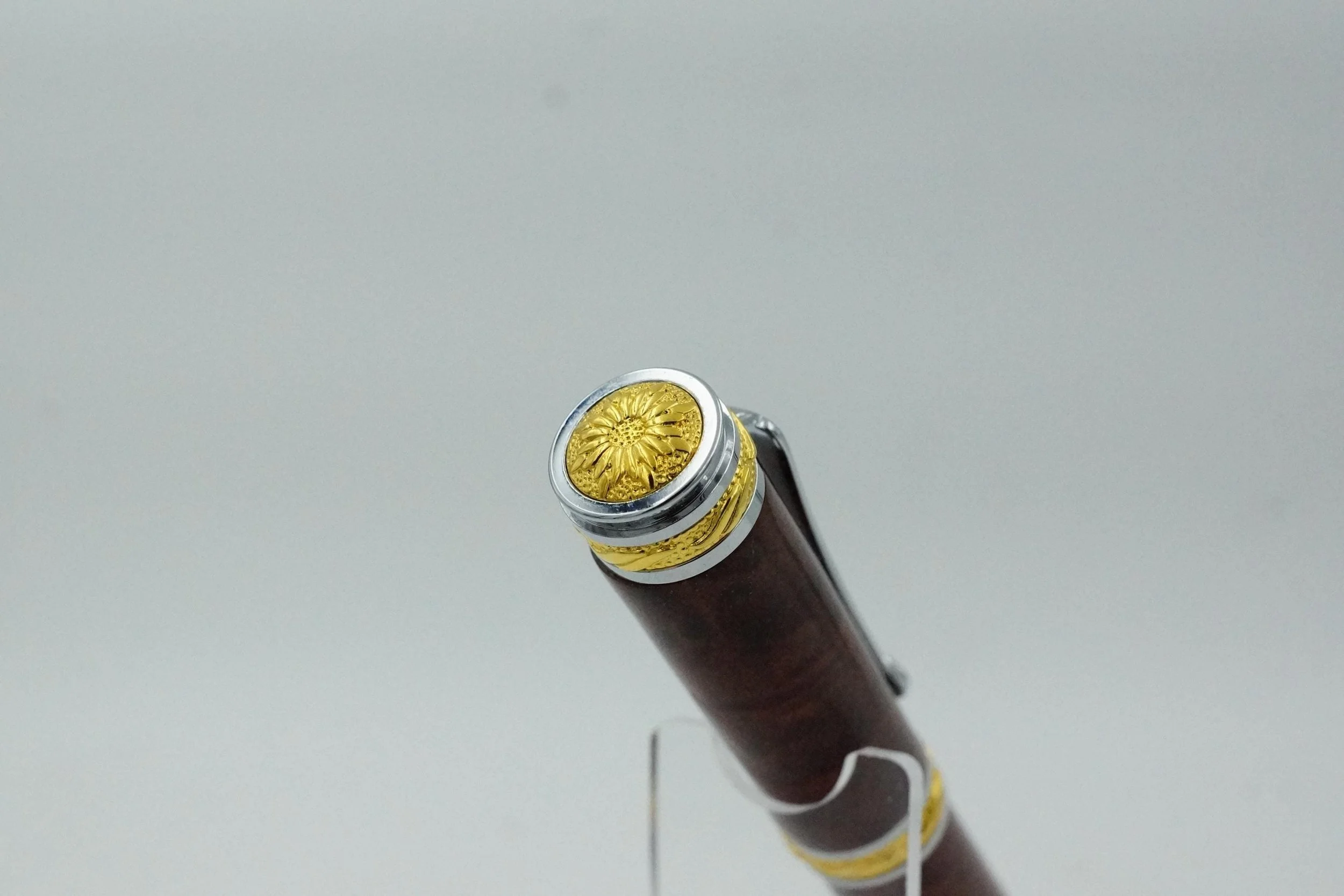 Close-up of a vintage fountain pen with gold and silver embellishments, resting on a stand against a plain white background.