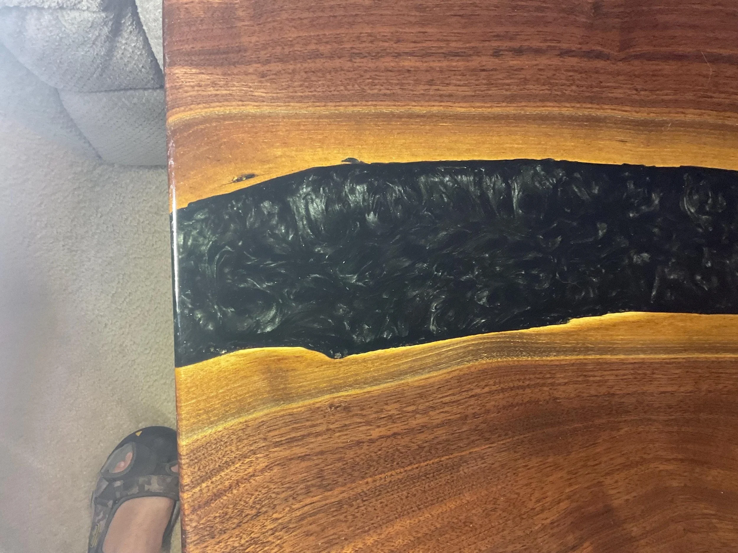 Close-up of a wooden surface with a black, textured, resin-filled inlay in the center.