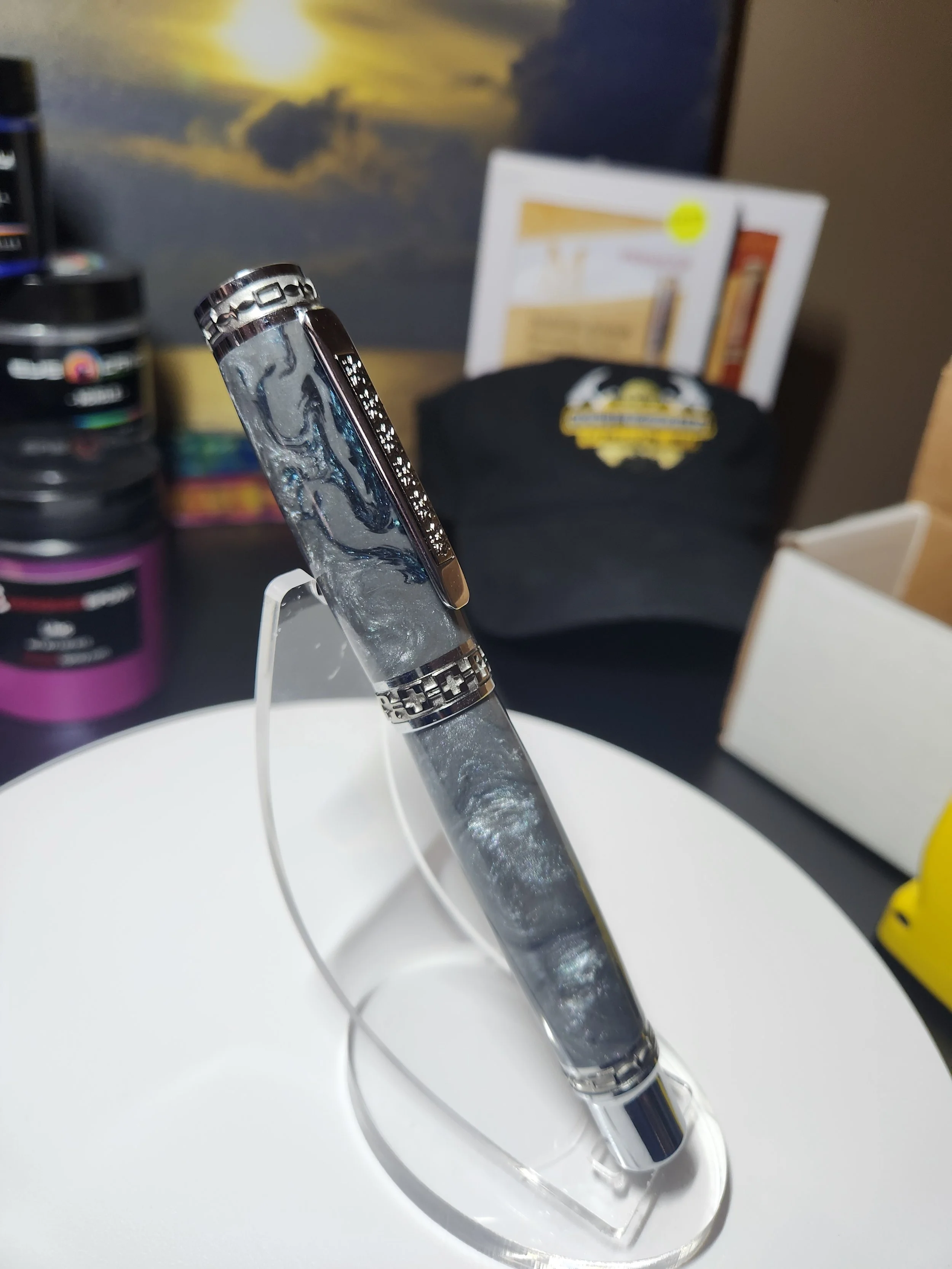 Close-up of a luxury ballpoint pen with a marbled gray and black design, displayed on a white stand in a store or display area.