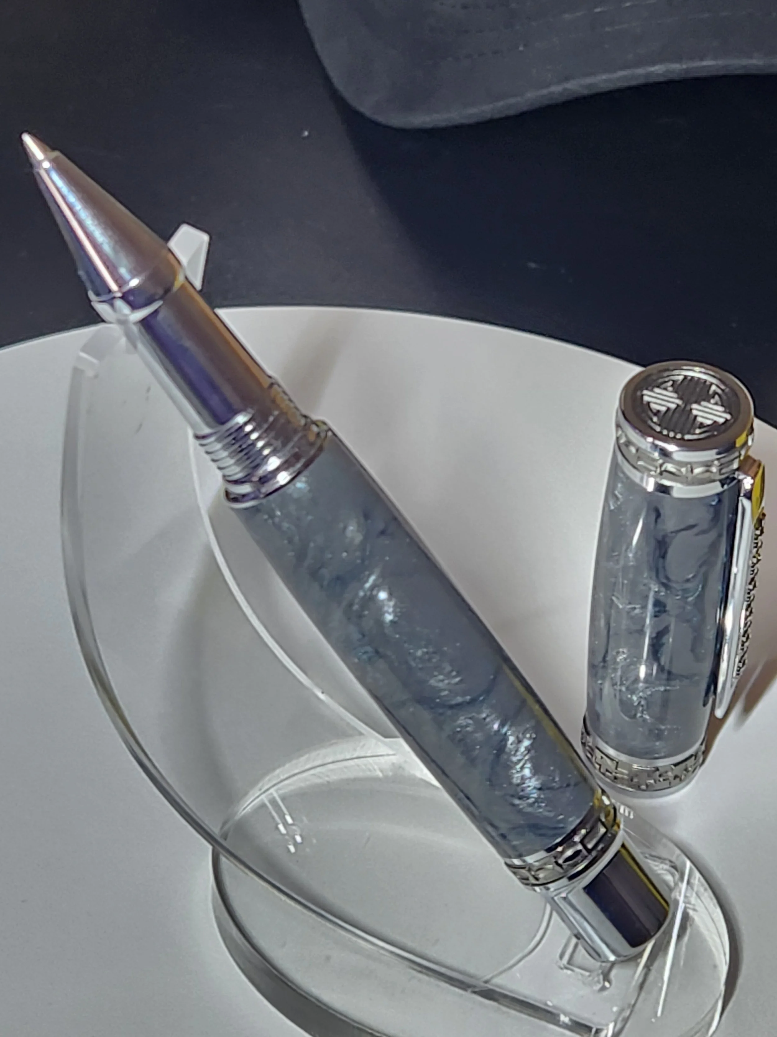 A silver pen and a clear lighter on a white rectangular stand, with a dark background.
