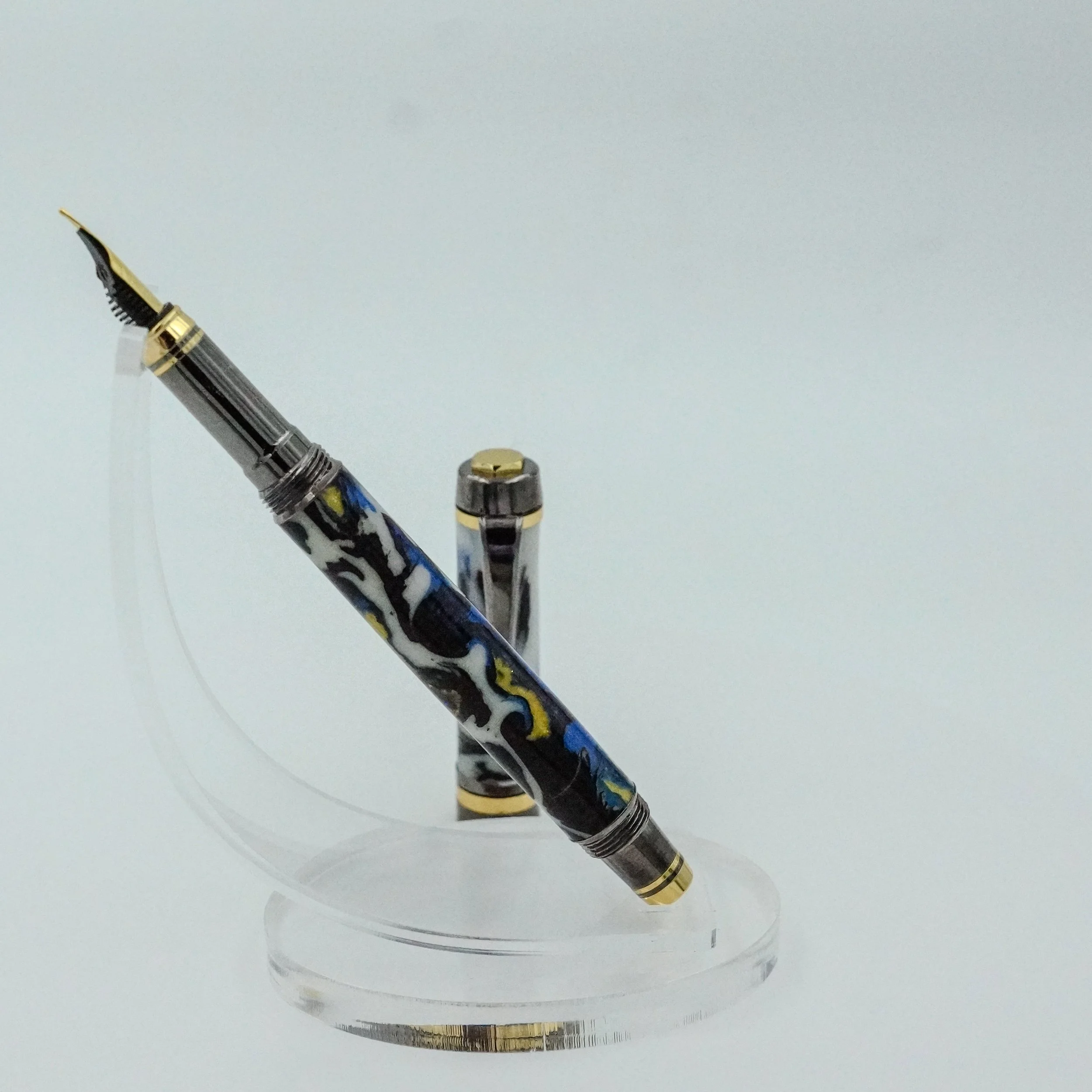 A luxury fountain pen with a colorful marbled design on the body, gold accents, and a black nib, displayed on a clear stand with the cap removed.