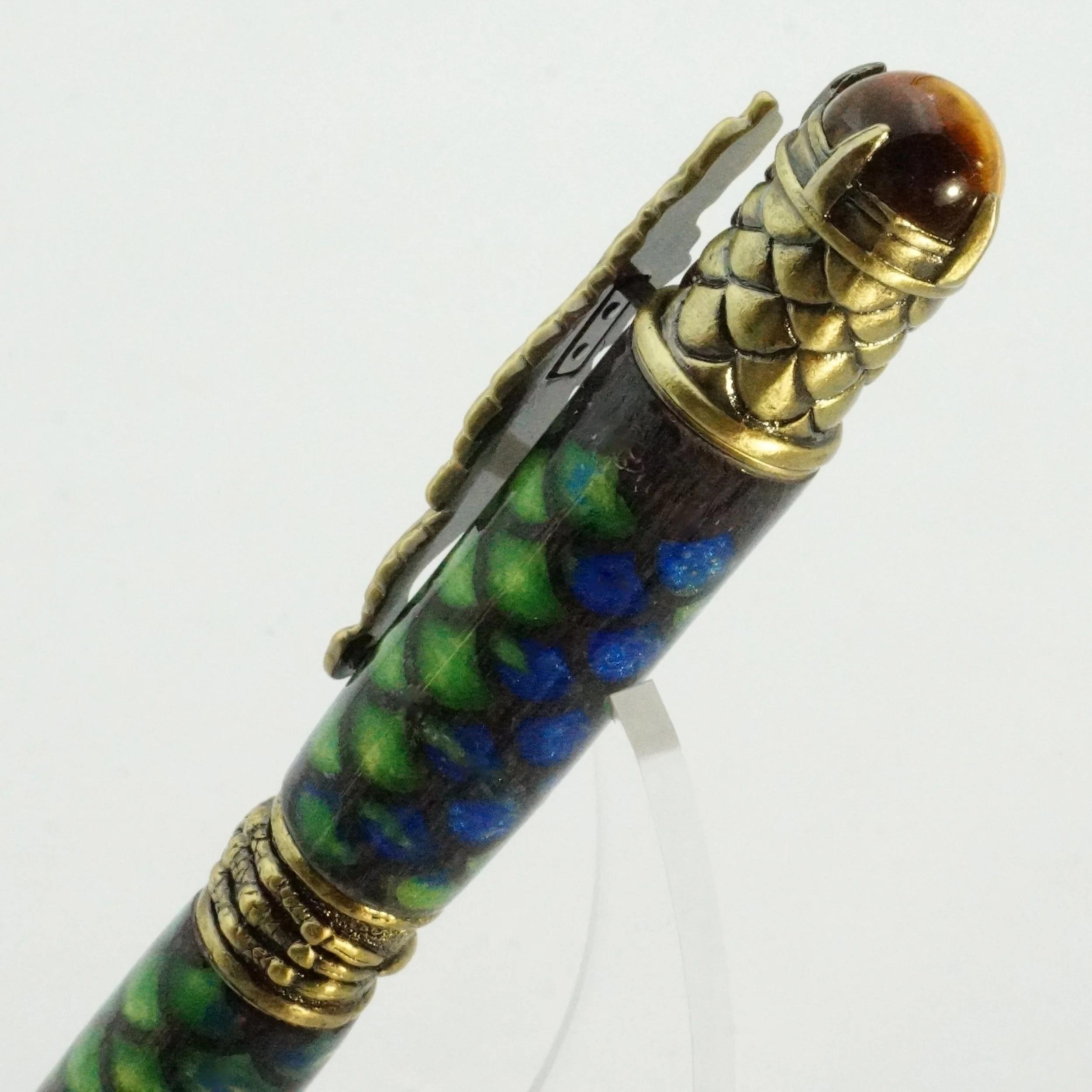 Close-up of a decorative pen with a golden dragon head design on the top, featuring blue and green stones embedded in the body.