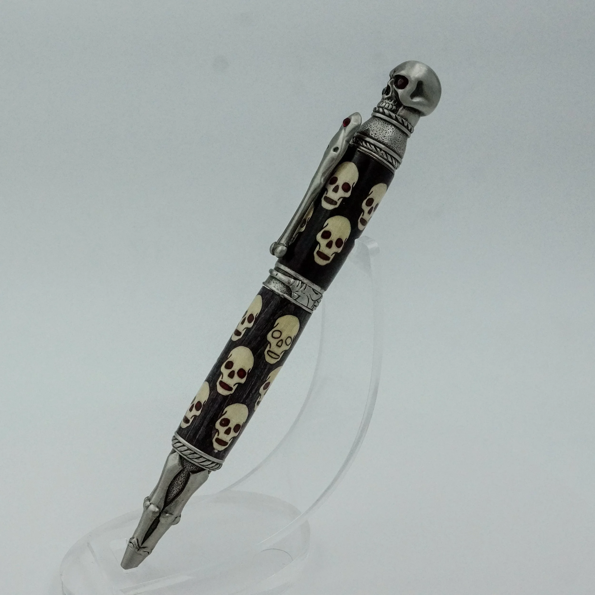 Decorative pen with skull and skull pattern design, featuring silver accents and a skull tip, displayed on a clear stand.