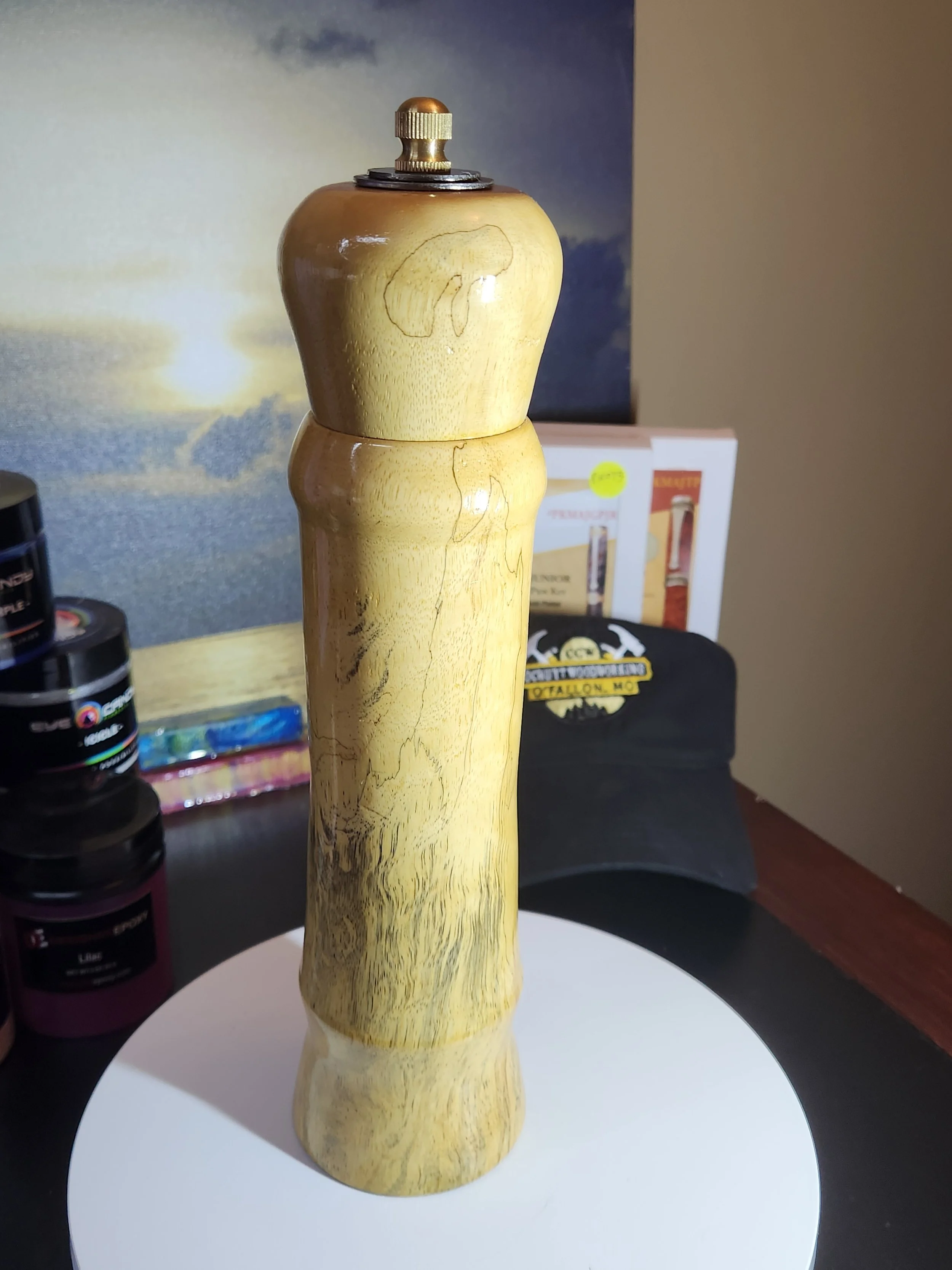 Wooden pepper mill with a metal top on a white circular surface.
