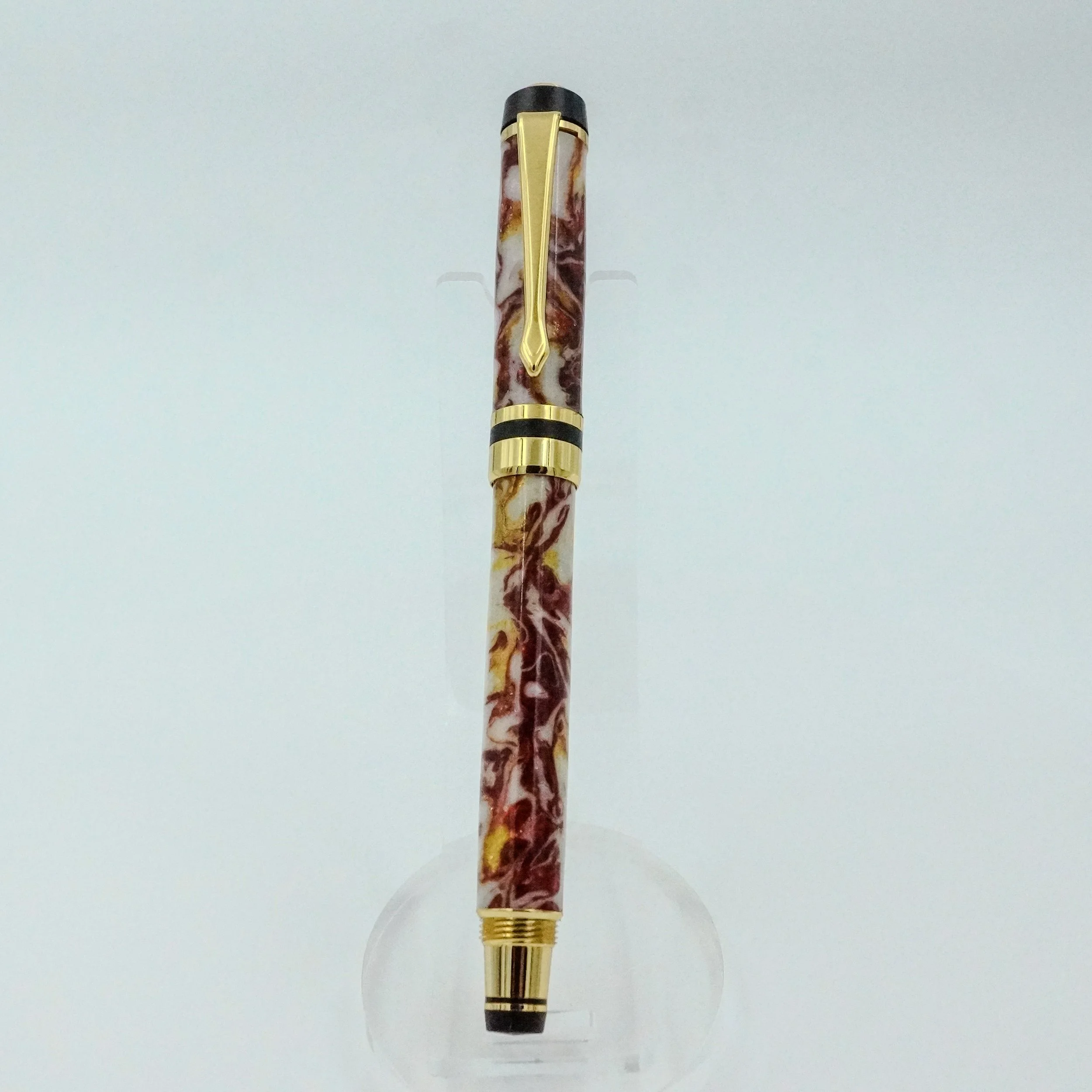 A marbled resin and gold-accented fountain pen displayed vertically on a clear stand against a white background.