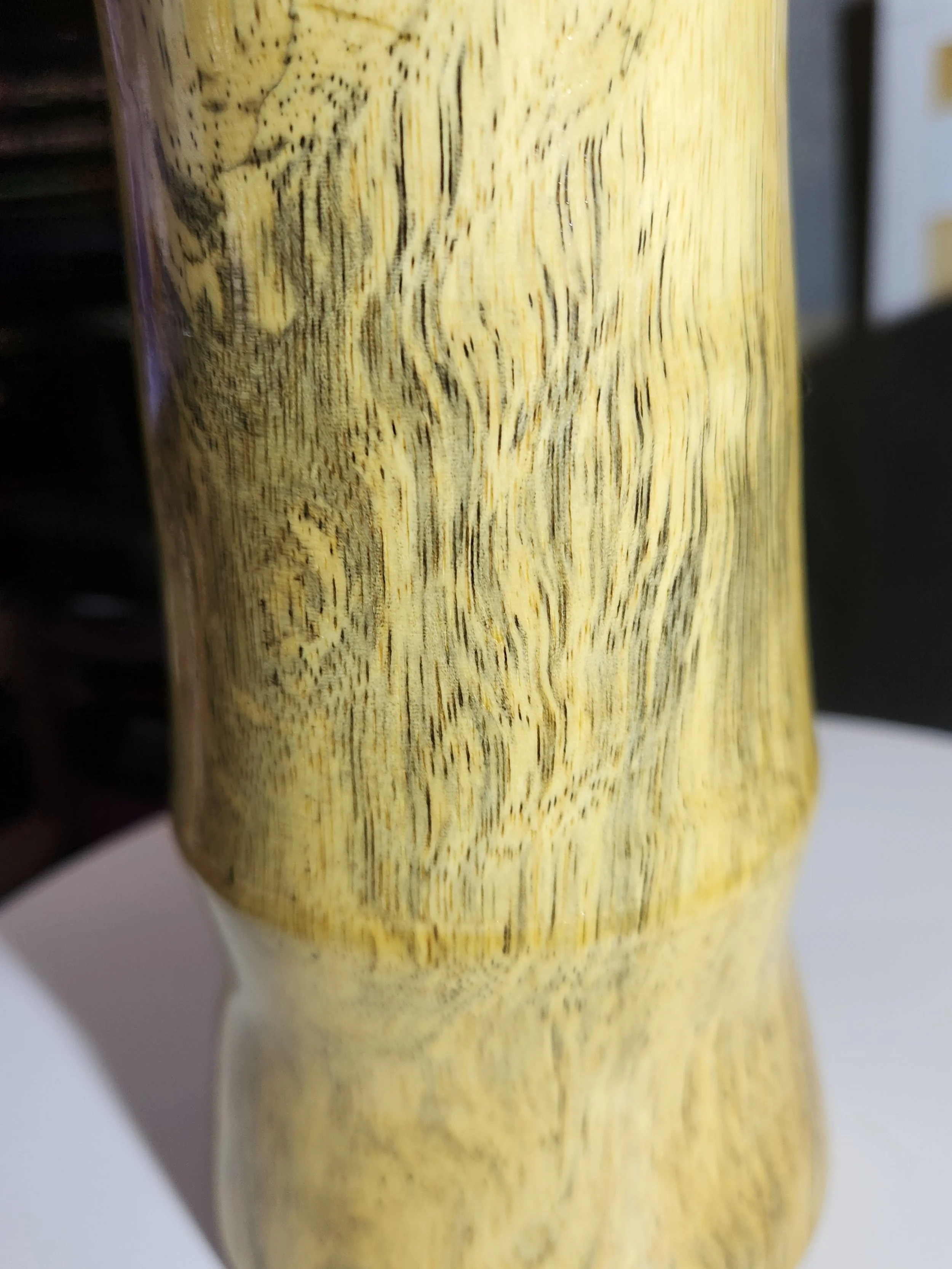 Close-up of a wooden object with a smooth, light-colored finish and visible wood grain pattern.