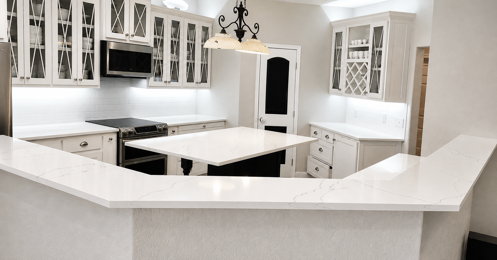 A modern kitchen with white cabinetry, a center island, white countertops with gray veining, a black stove, a microwave, and organized glass-front cabinets, illuminated by natural light and a black chandelier.