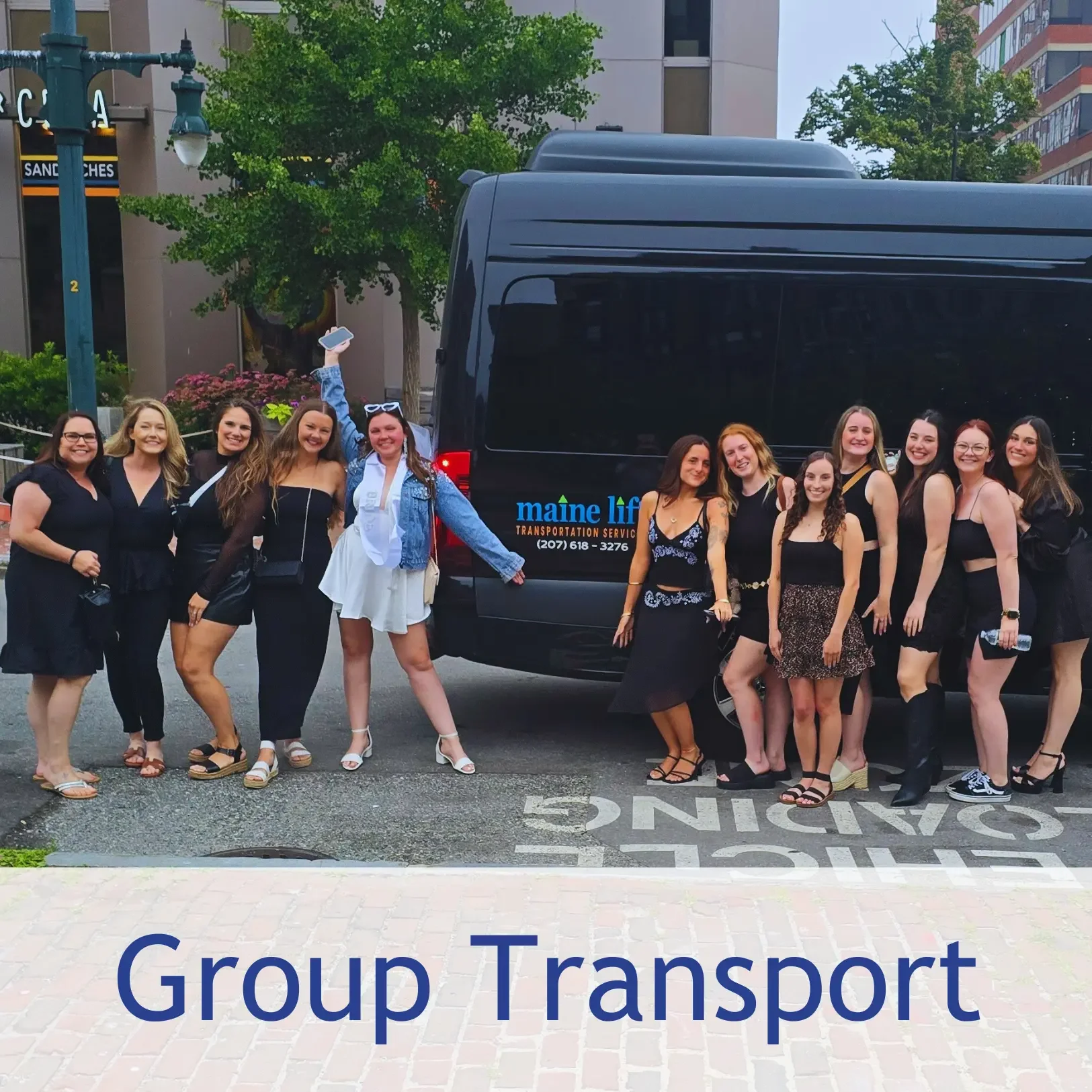 A group of women posing in front of a black transportation van labeled 'maine life transportation service' on a city street with trees and buildings in the background.