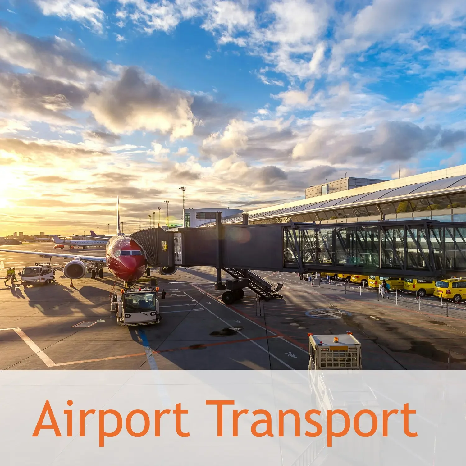 View of an airport tarmac with a red airplane connected to a jet bridge during sunset, with several passenger buses and airport staff visible, under a sky with scattered clouds.