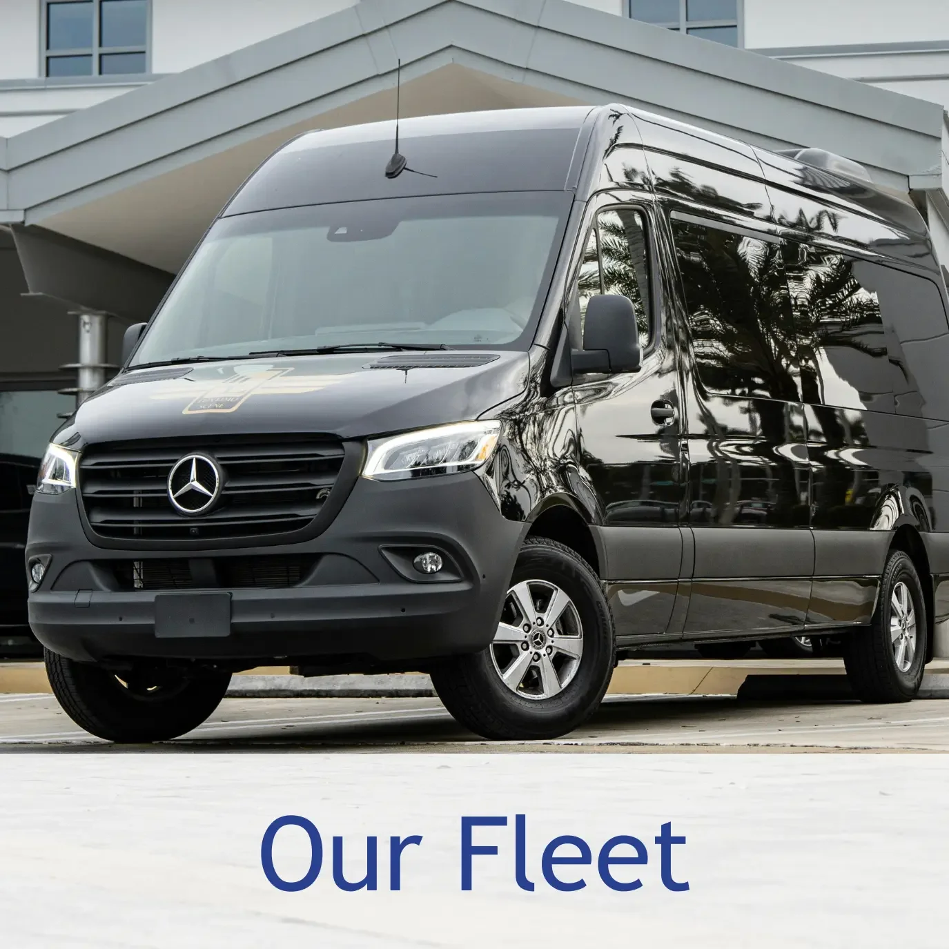 Black Mercedes-Benz van parked outside modern building with trees reflected on its surface, with the text 'Our Fleet' at the bottom.