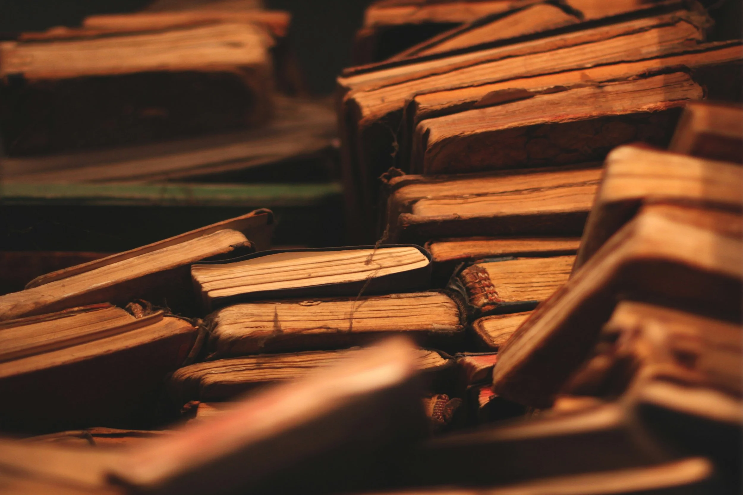 Close-up of old, worn books stacked on top of each other, with yellowed and battered pages.