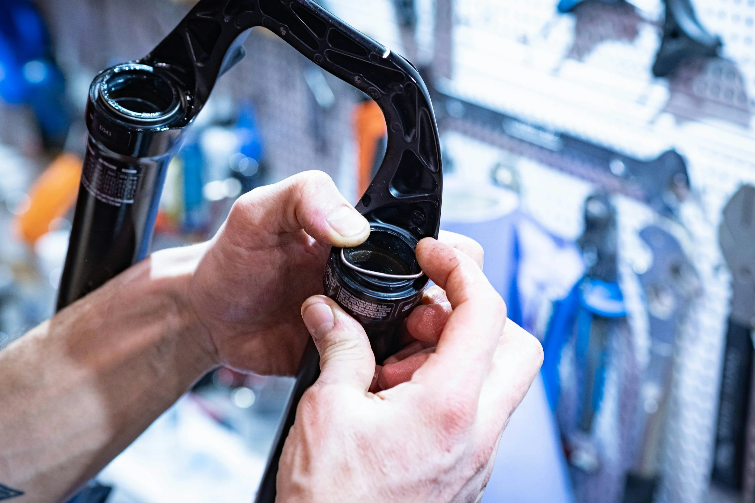 Person working on a mountain bike's suspension fork, inserting oil or lubricant into the fork's seal at a bike repair shop.