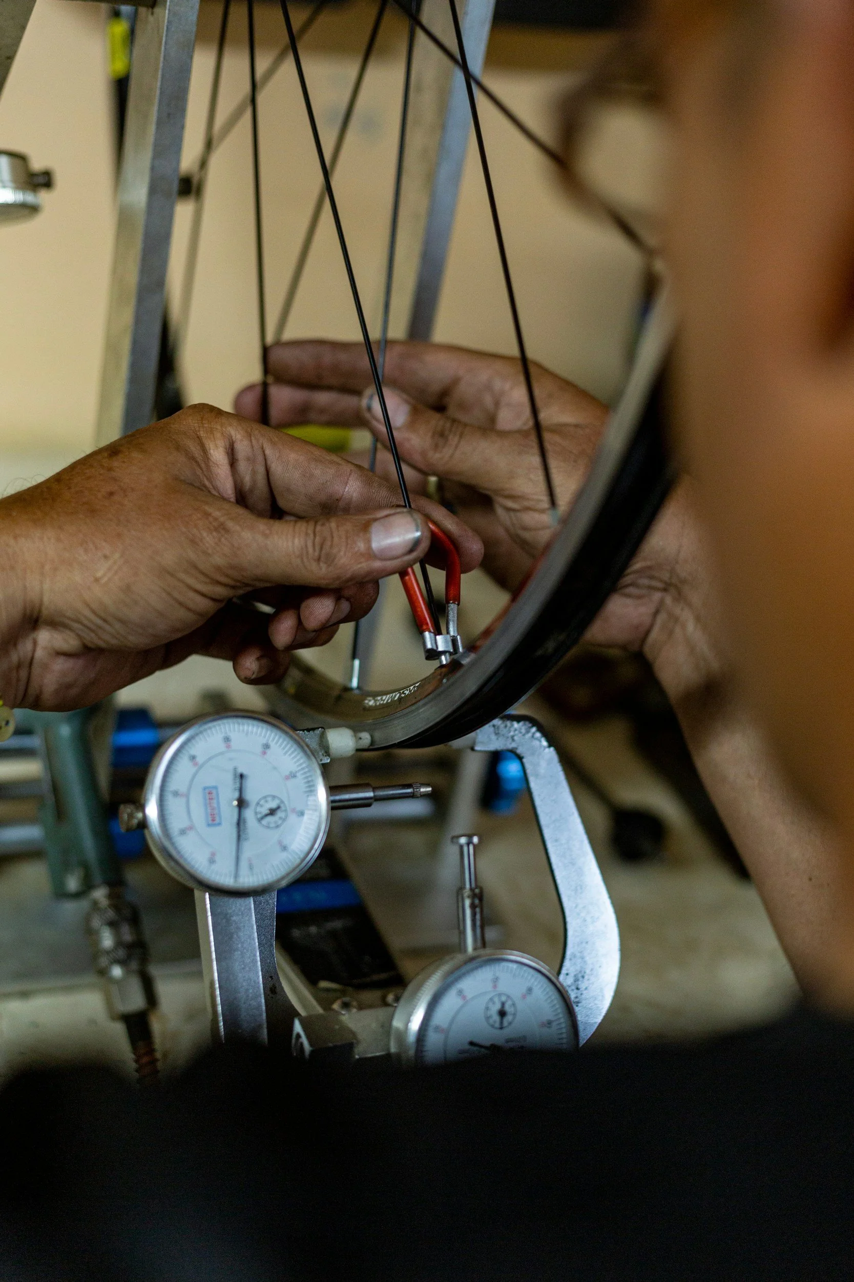 Person working on a bicycle wheel, using a gauge and tools for repair or maintenance.