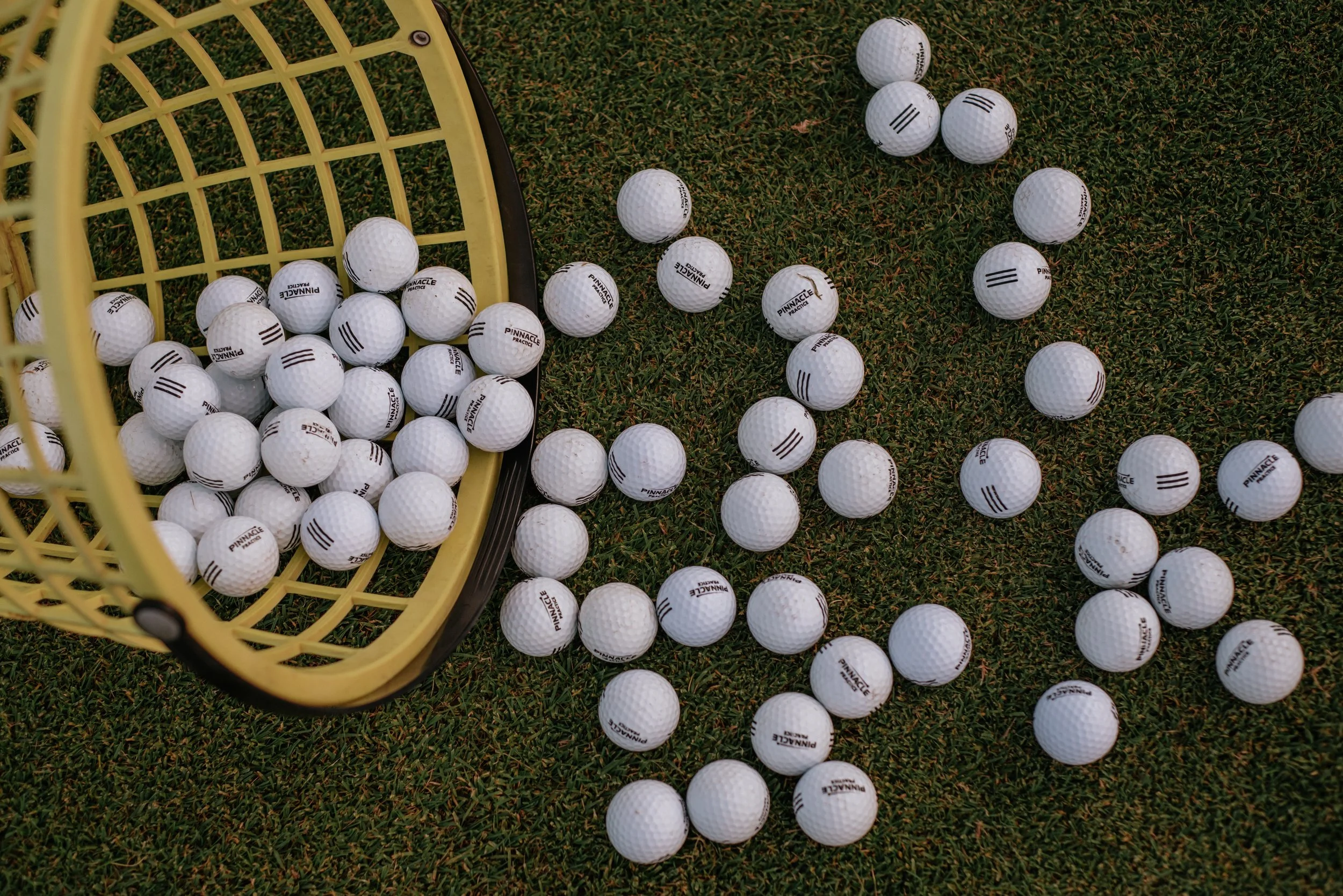 A yellow plastic basket tipped over with white golf balls spilling onto grass.