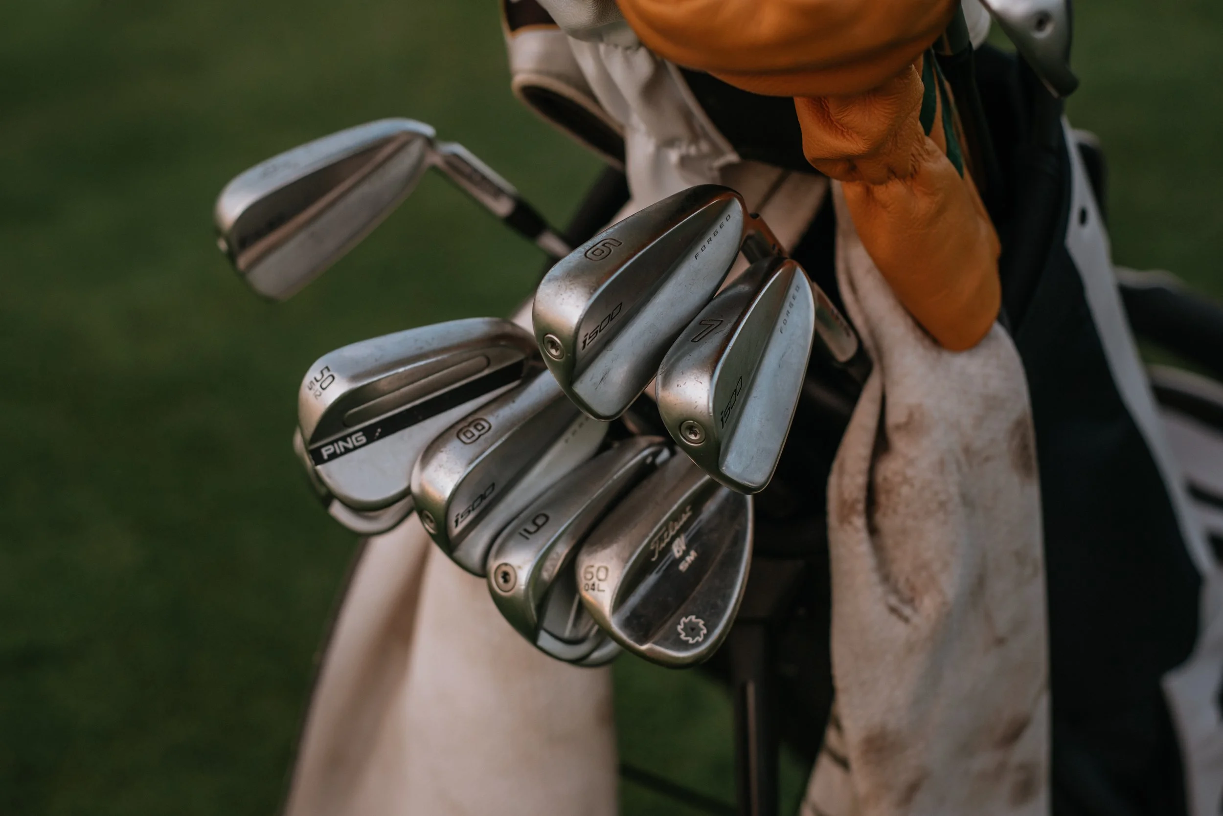 Close-up of a golf bag with several golf clubs, including irons and wedges, on a golf course.