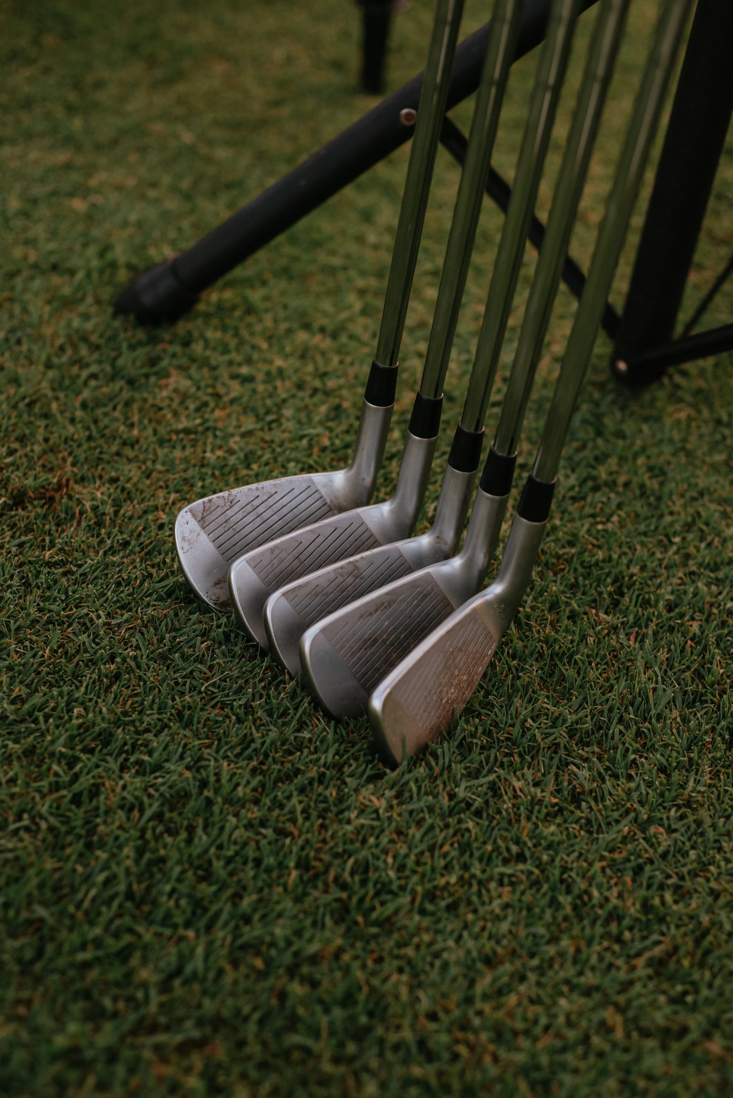 Four golf clubs leaning against a black stand on a grassy surface.