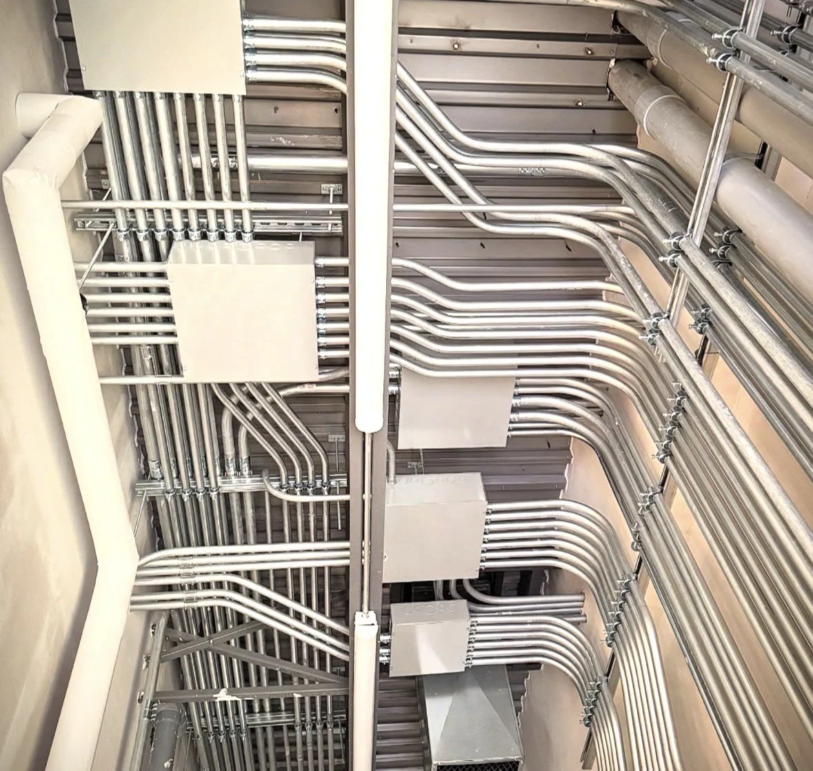 Ceiling with organized metal electrical conduits and junction boxes in an industrial or commercial setting.