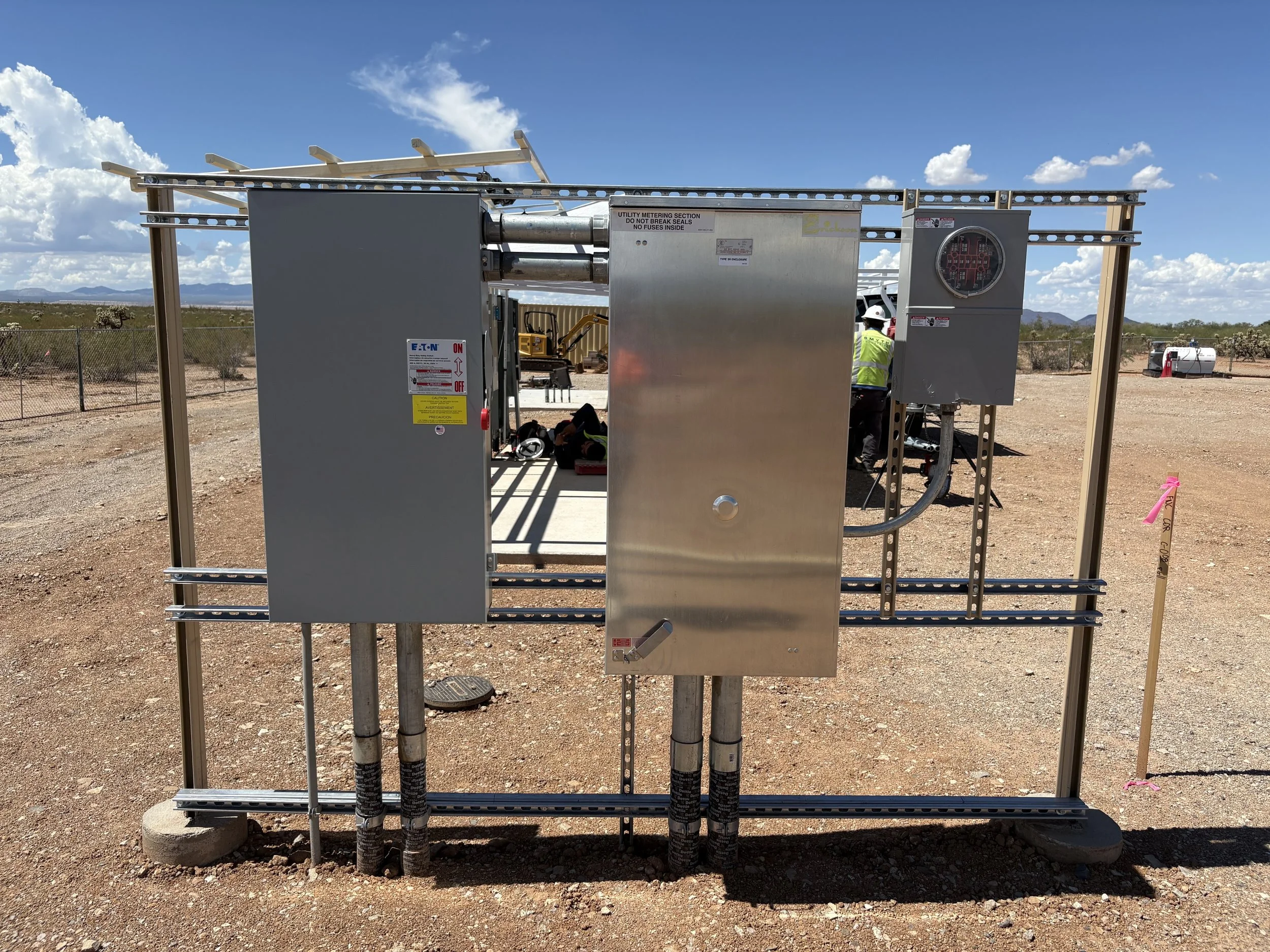 Electrical equipment and control panel at an outdoor site with desert landscape and blue sky.