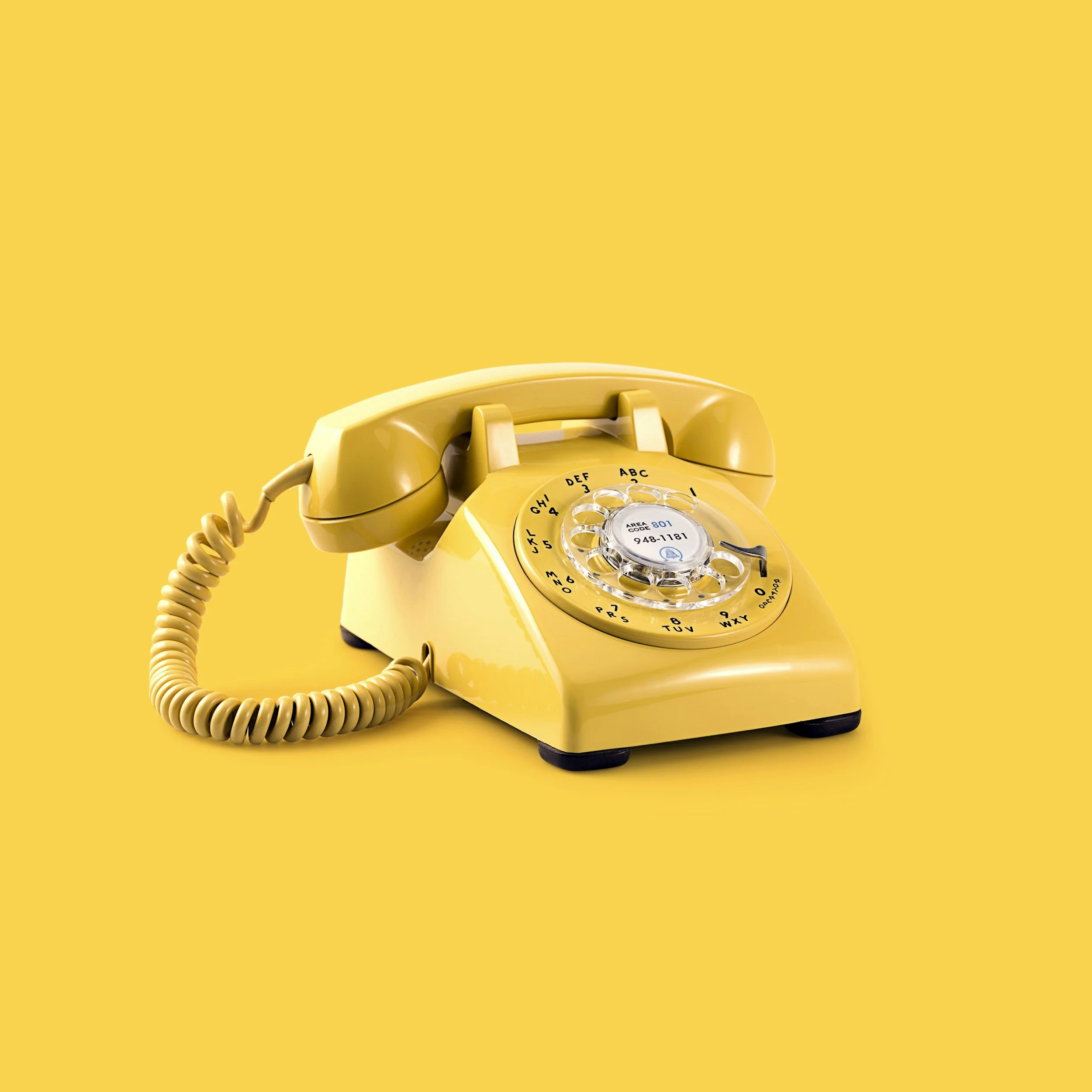 Close-up of a vintage yellow rotary telephone against a yellow background.