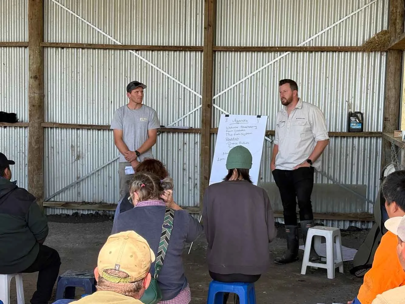 Two of the Agrownomics team standing in front of a small group, giving a presentation inside a farm shed, with a whiteboard behind them and several seated people listening.