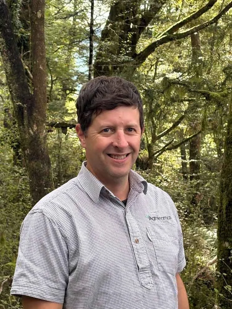 Jeffrey Lamb Agrownomics Operations Manager, smiling outdoors in a green forest setting with trees and sunlight filtering through the branches.