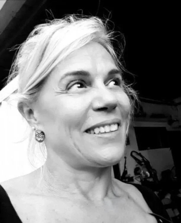 Retrato em preto e branco de uma mulher sorrindo com cabelo claro preso, usando brincos e uma blusa regata preta.