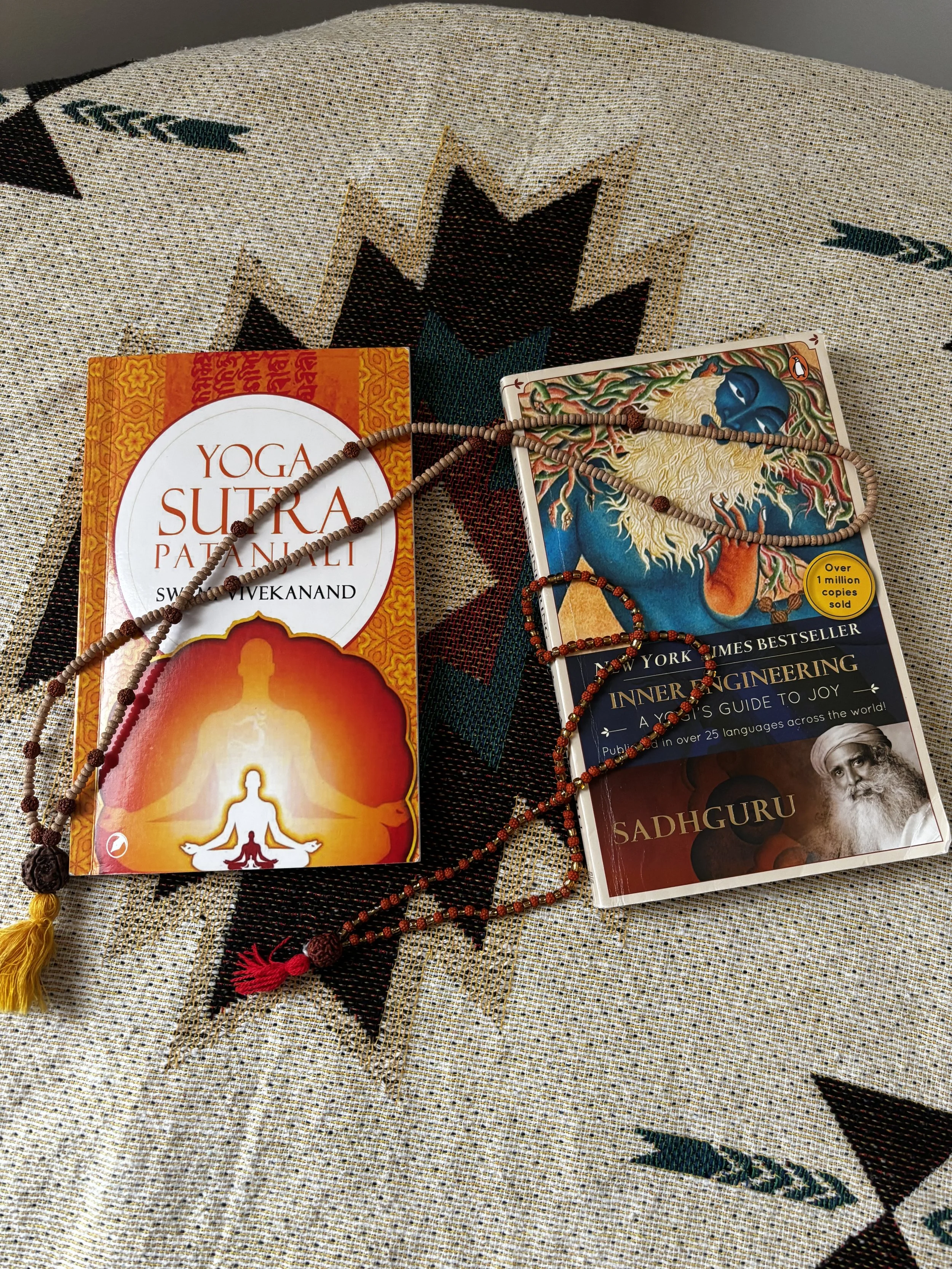 Two books about yoga and spiritual topics along with prayer beads and necklaces on a decorative cloth surface.