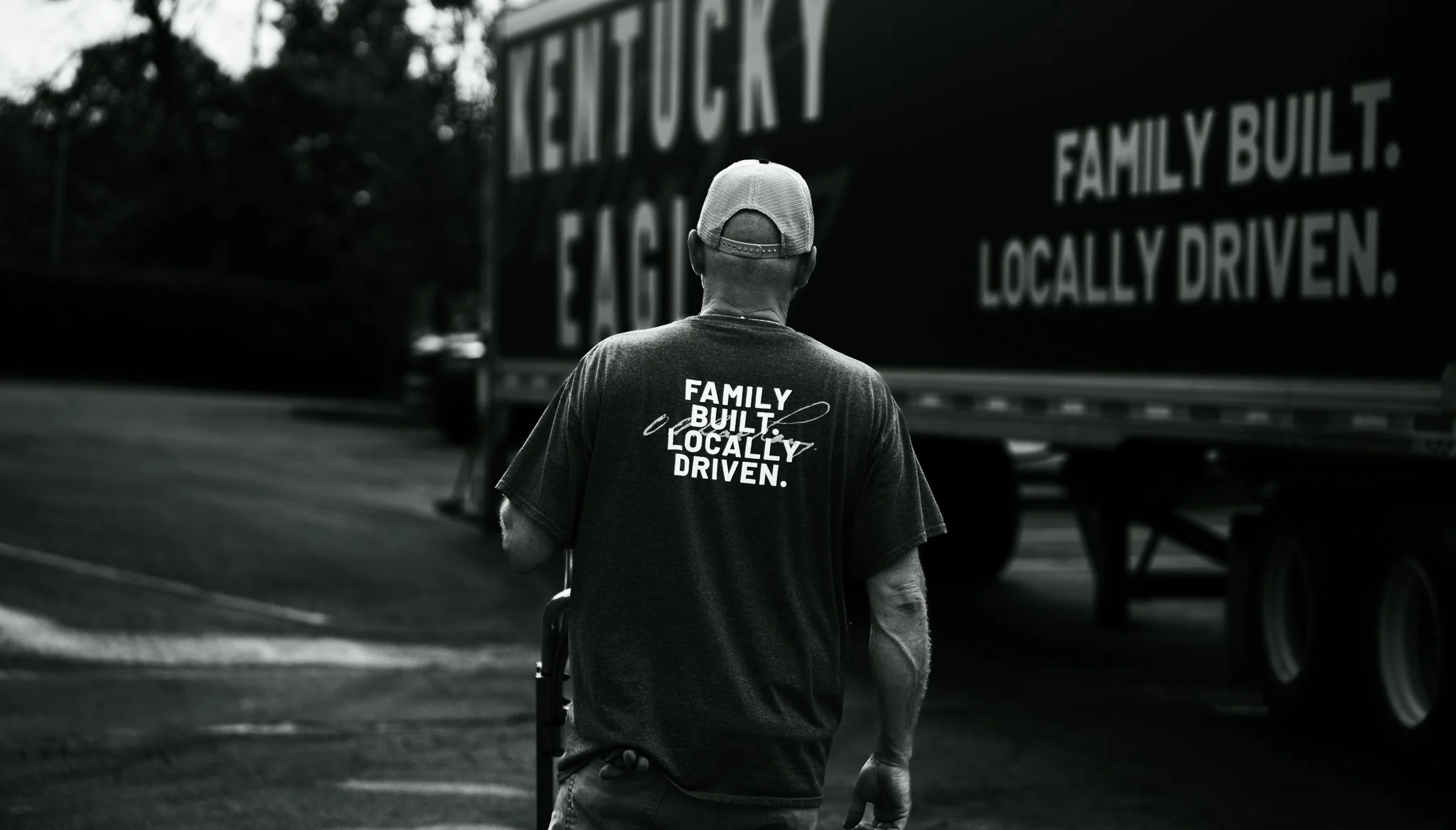 A man wearing a cap and T-shirt with the message "Family Built Locally Driven" walking near a truck with the same message.
