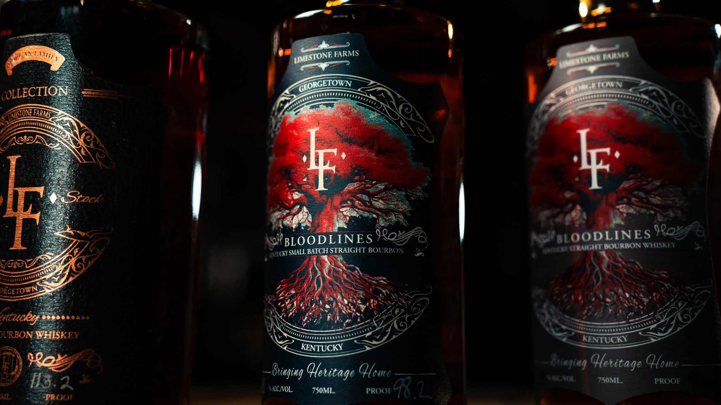 Three bottles of Bloodlines Kentucky straight bourbon whiskey on a dark background, with the middle bottle featuring a tree with red leaves and roots on the label.