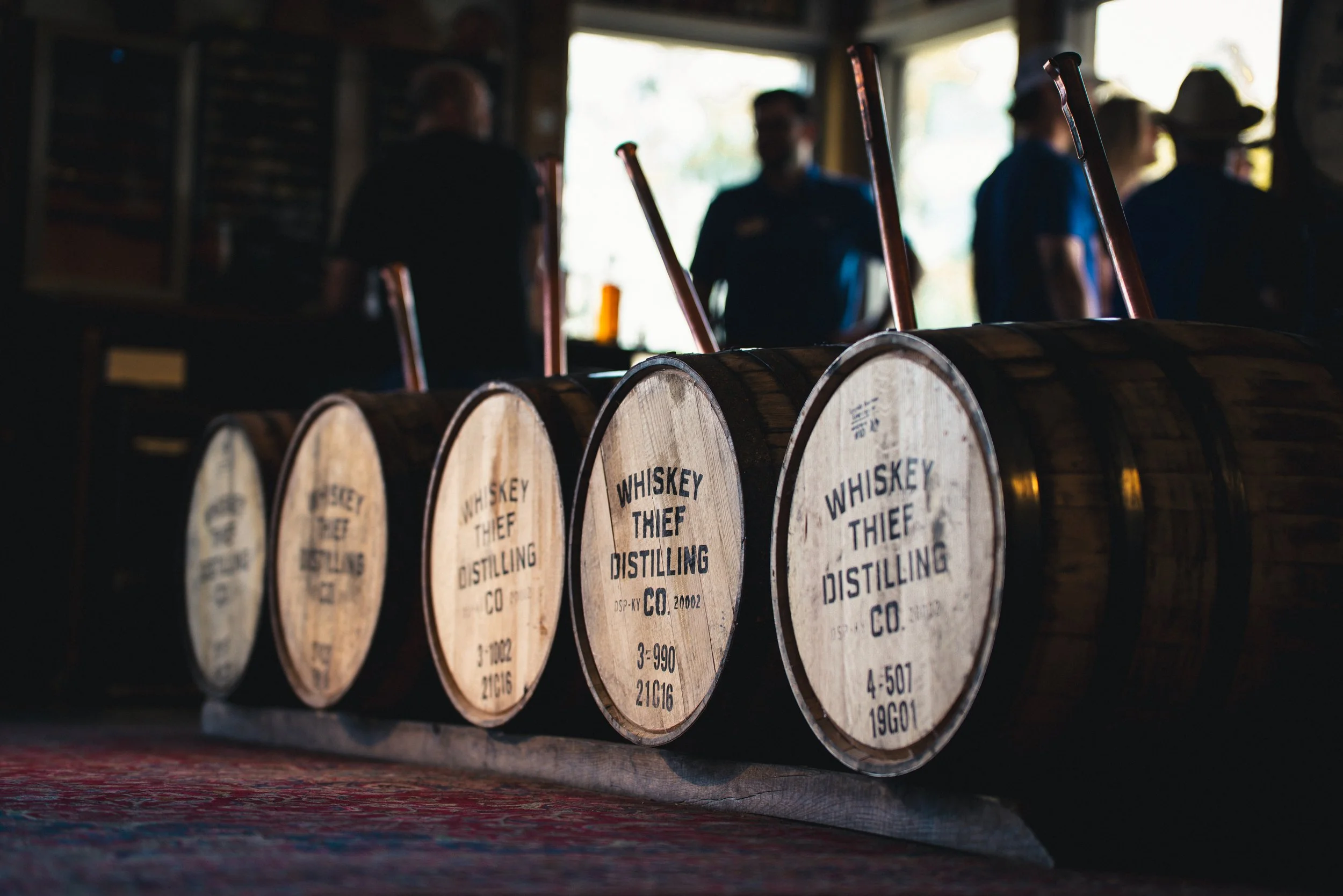 A row of small whiskey barrels with the label 'Whiskey Thief Distilling Co.' on a wooden surface in a dimly lit room.