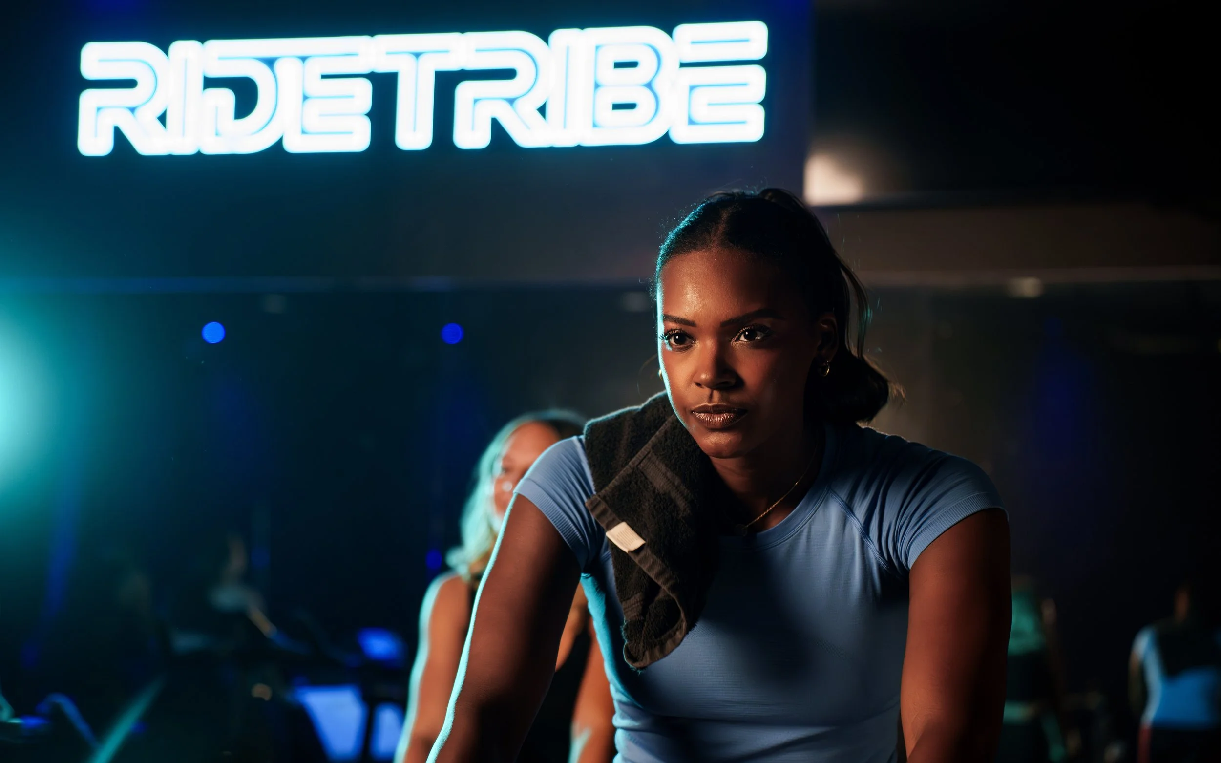 A woman working out in a gym with neon RIDE TRIBE sign in the background