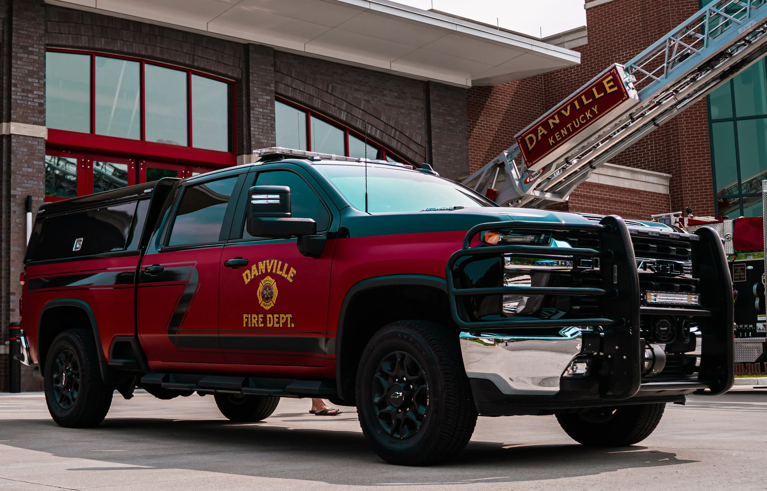 A black and red fire department pickup truck parked outside a fire station with a ladder, with the sign 'Danville Kentucky' on it.