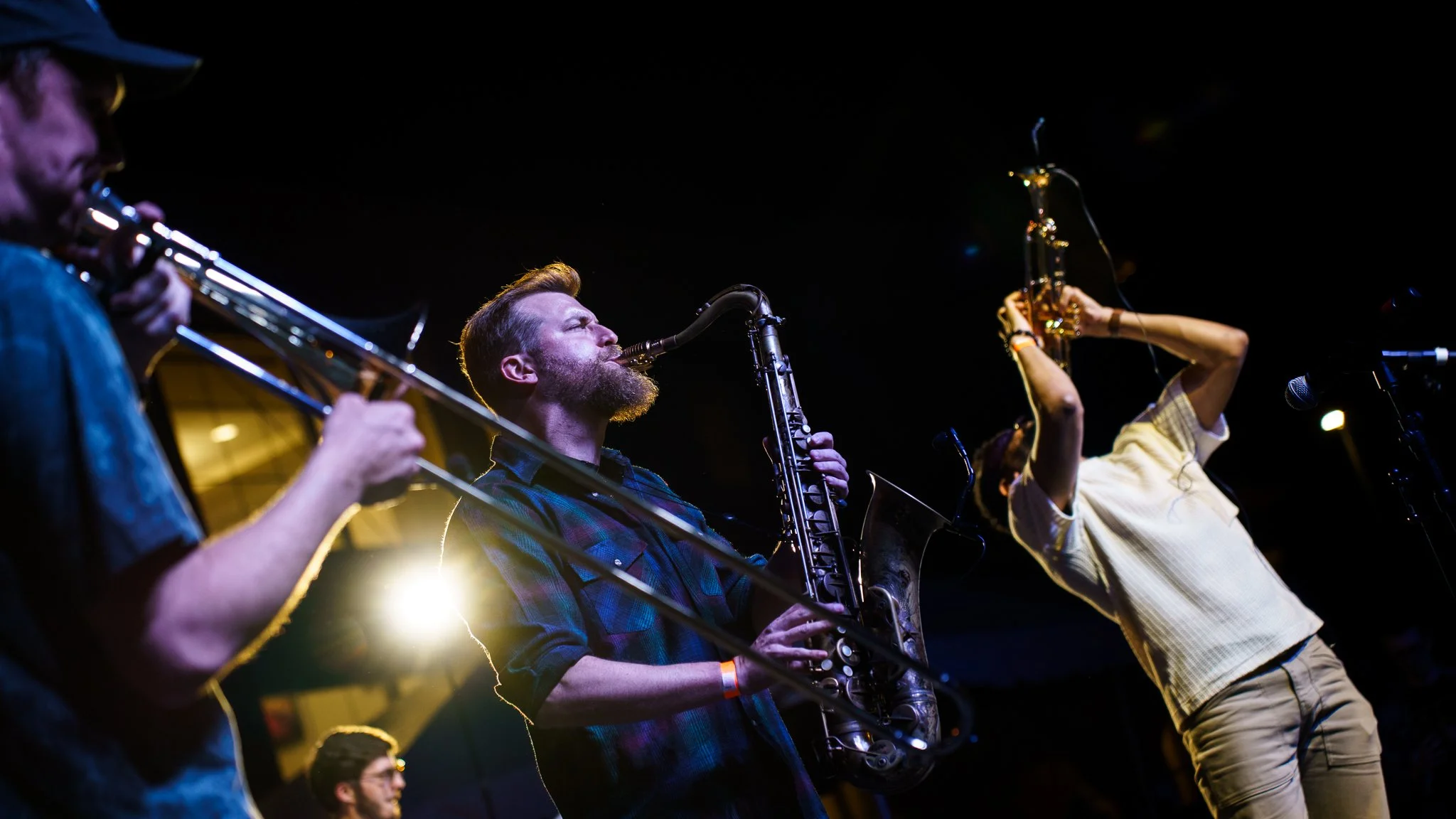 Musicians performing on stage, playing saxophone and trumpet under stage lighting.