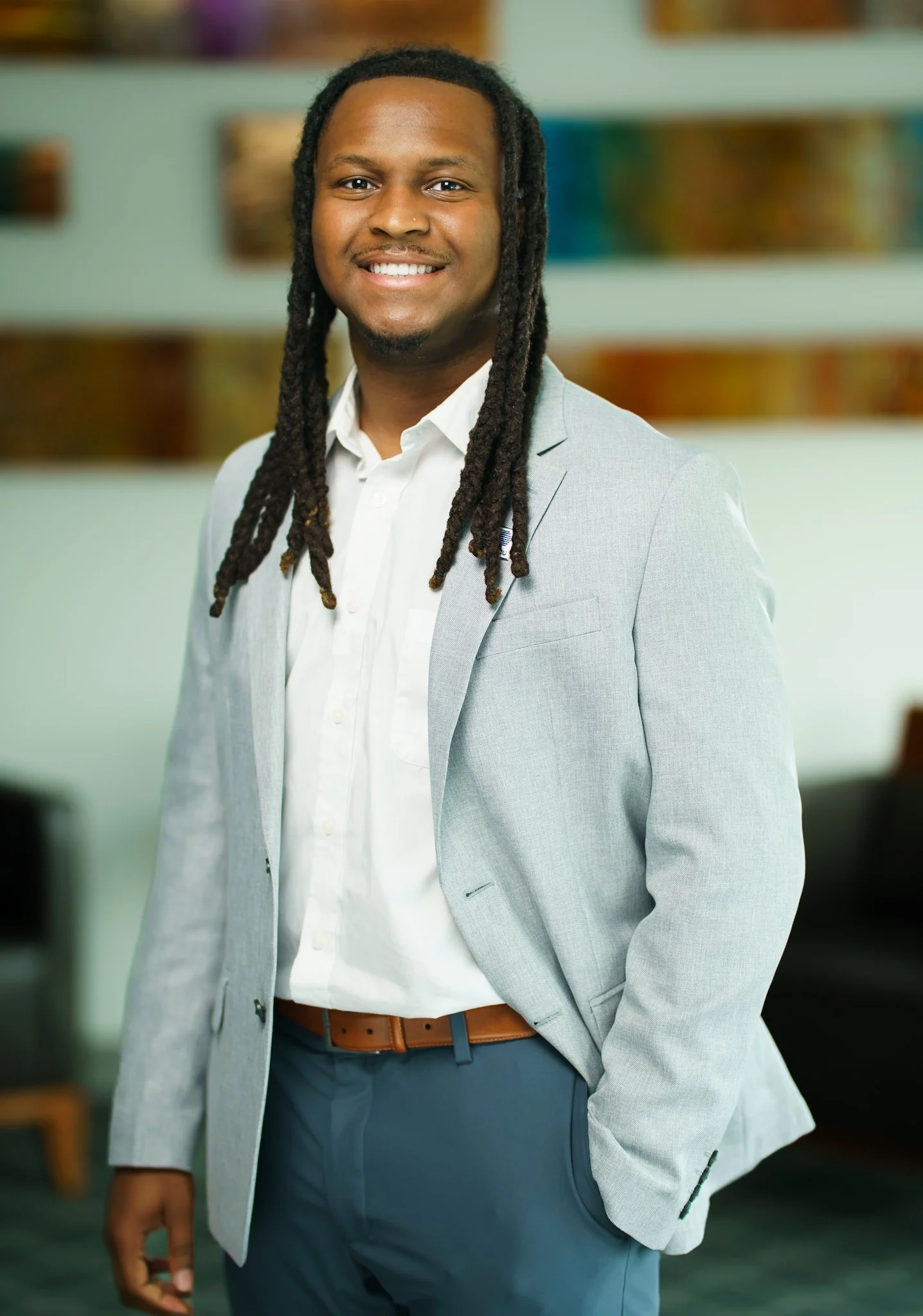 A man in a light gray blazer and white shirt smiling in an office setting.