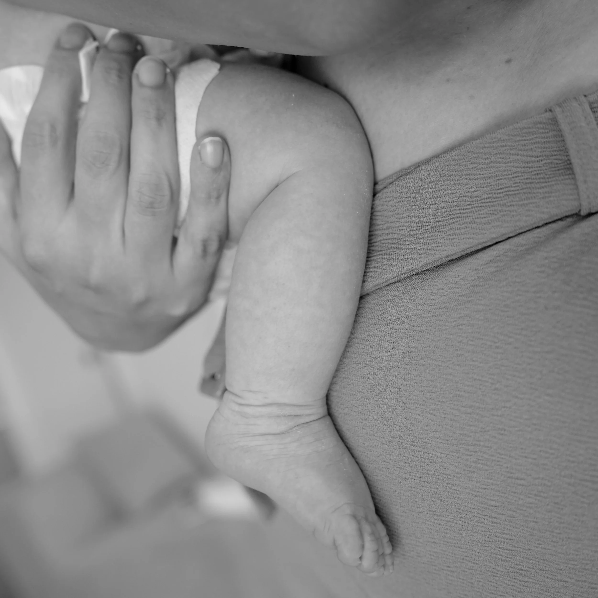 Black and white photograph of a person's hand with long fingernails resting on a person's knee, with part of their clothes visible.