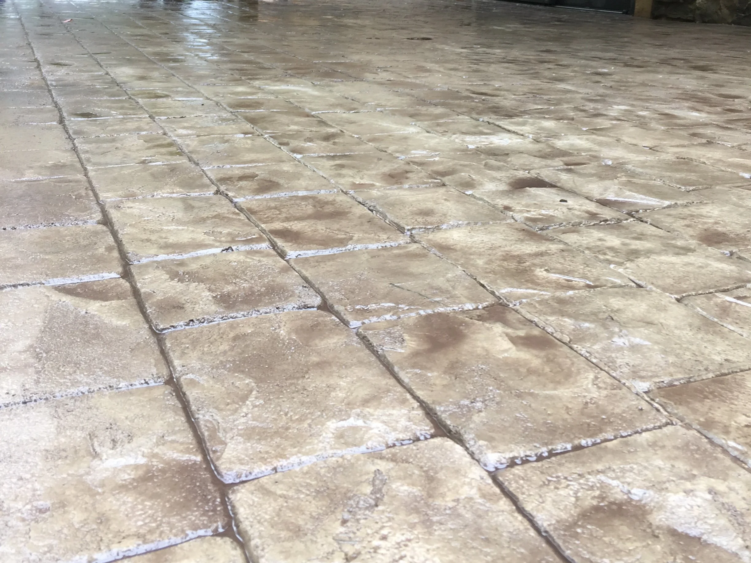 Close-up view of beige stone pavers on a floor, some with white residue or dust, arranged in a grid pattern.