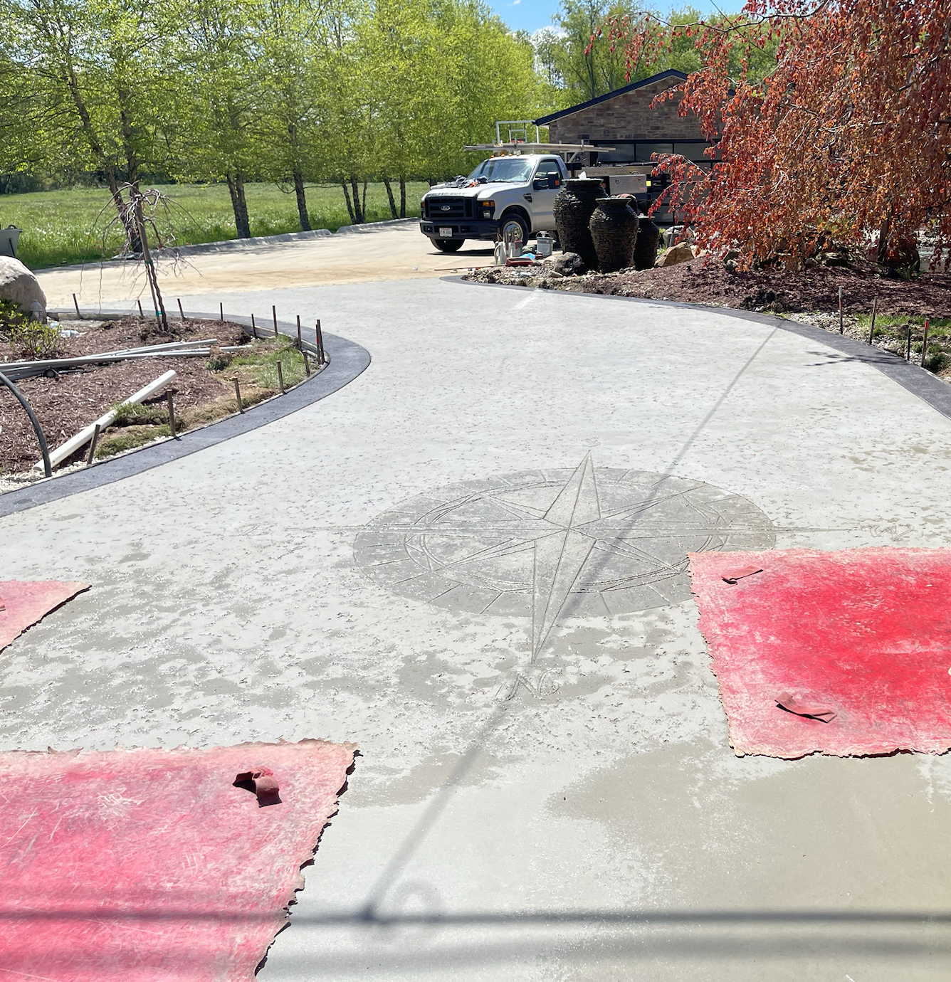 Newly poured concrete driveway with a compass design at the center, construction materials around, and trees in the background.