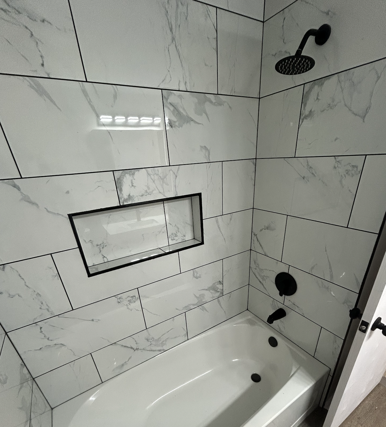 Modern bathroom with marble wall tiles, black fixtures, and a built-in niche in the shower wall.