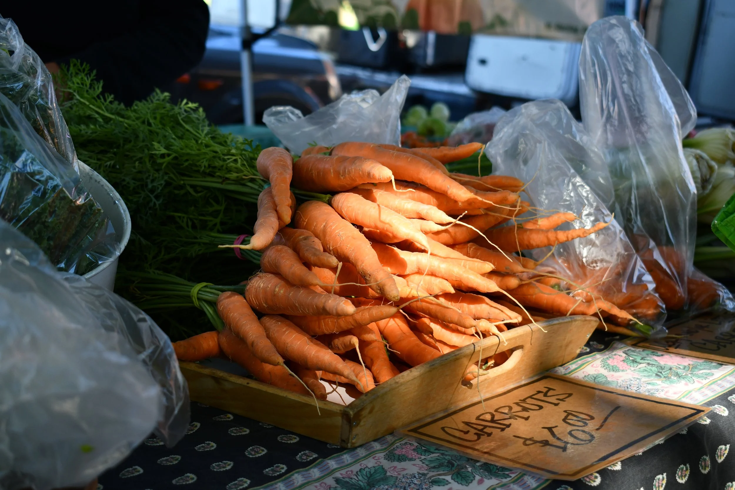 Fresh carrots displayed at a market stall with a handwritten sign indicating their price.