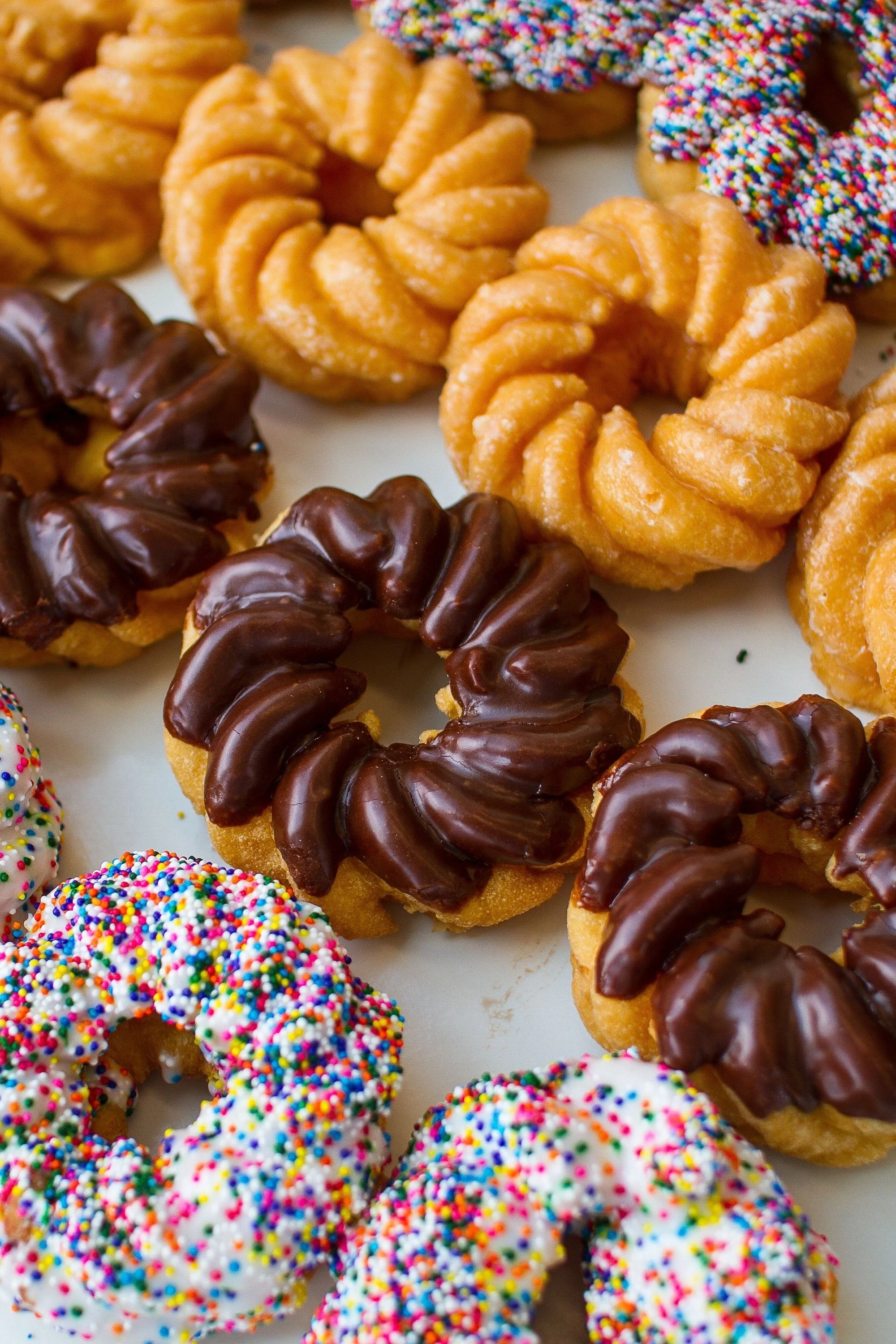 Assorted colorful donuts with sprinkles, chocolate glaze, and plain glazed flavors on a white platter.