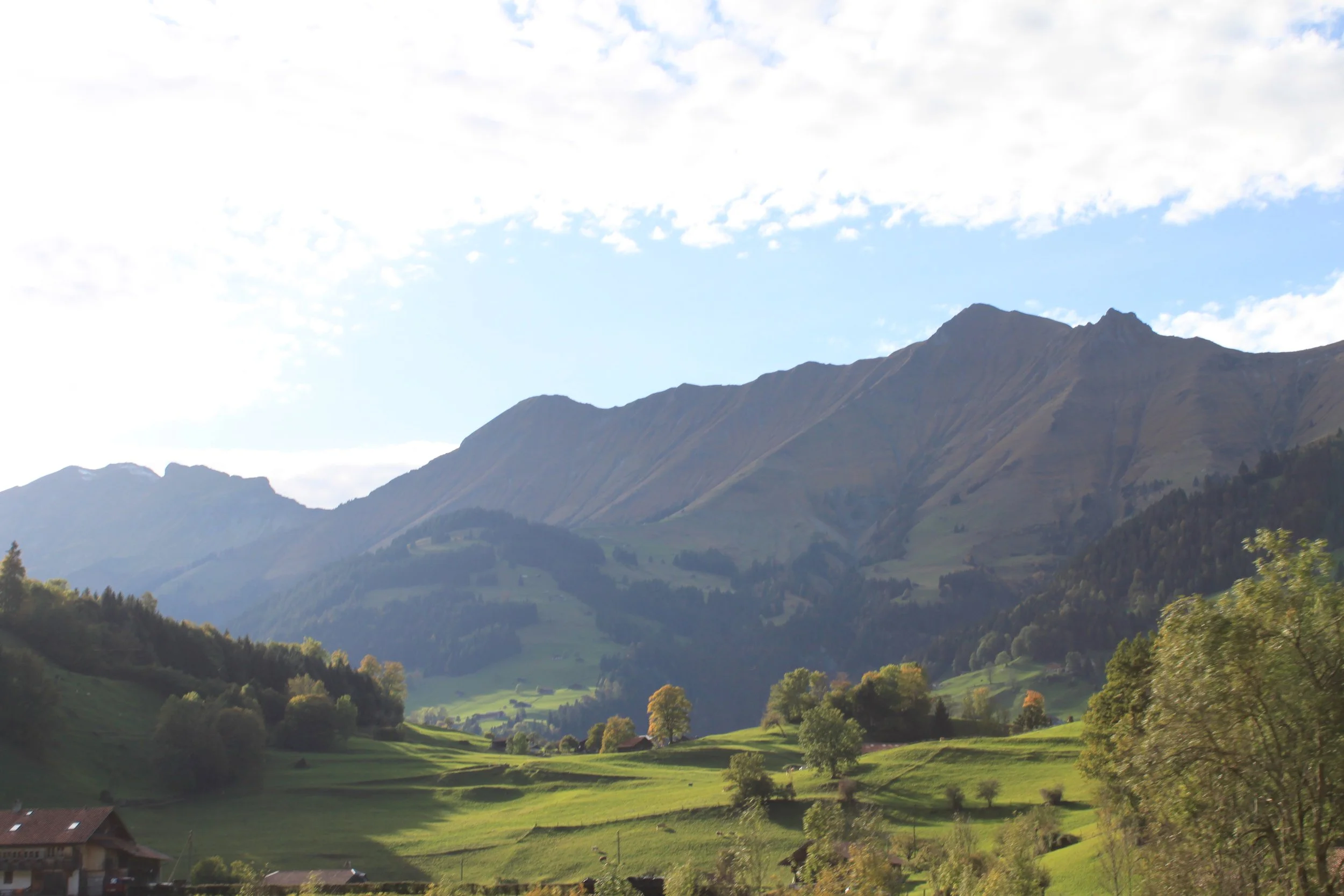 Scenic landscape of green rolling hills and mountains under a partly cloudy sky in daytime.