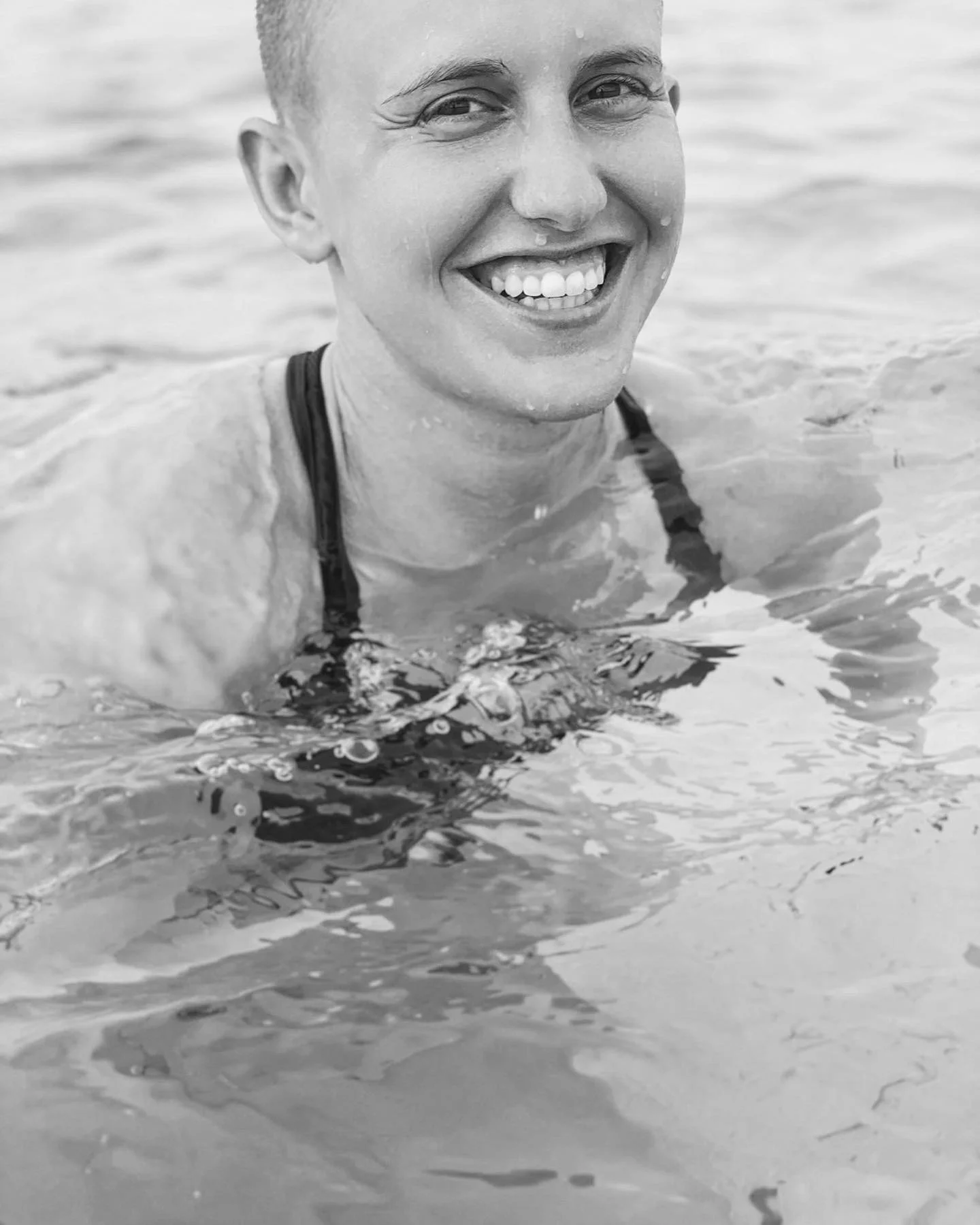 A woman smiling in water at the beach, wearing a swimsuit, with a happy expression.