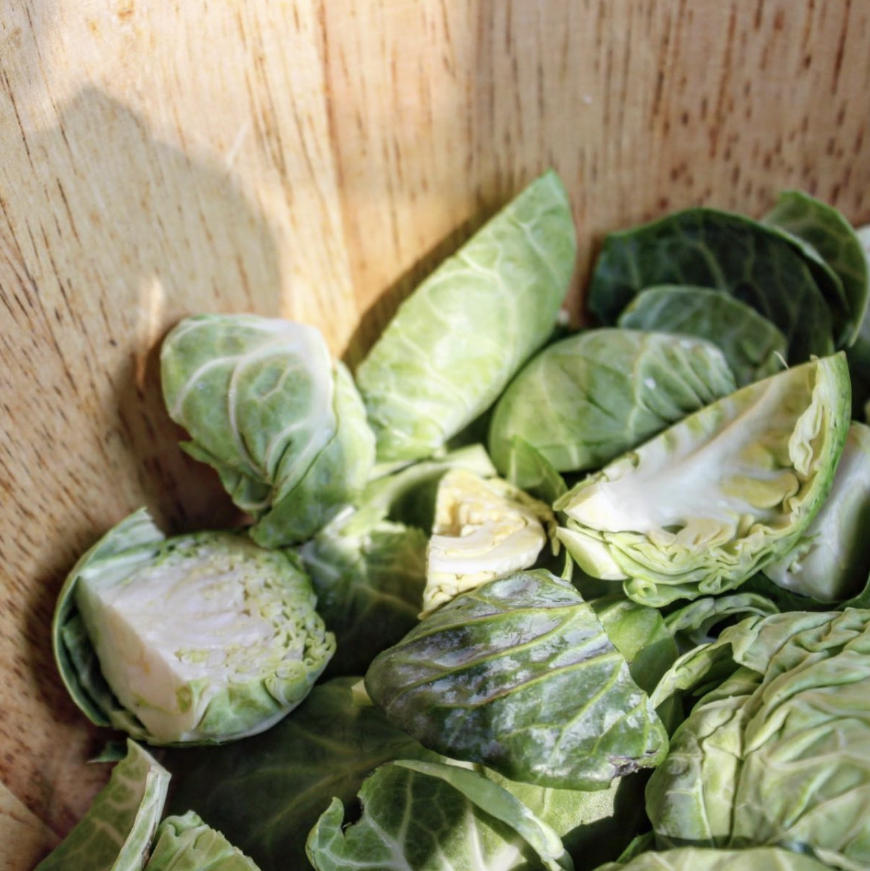 Brussels sprouts on a wooden cutting board, some cut open revealing the inner leaves.