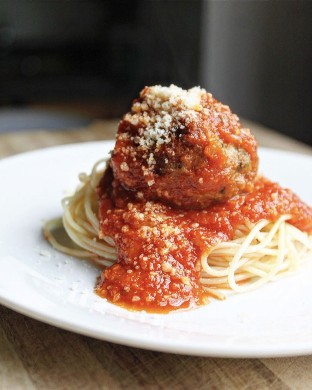 Spaghetti topped with two meatballs and grated cheese in tomato sauce on a white plate.