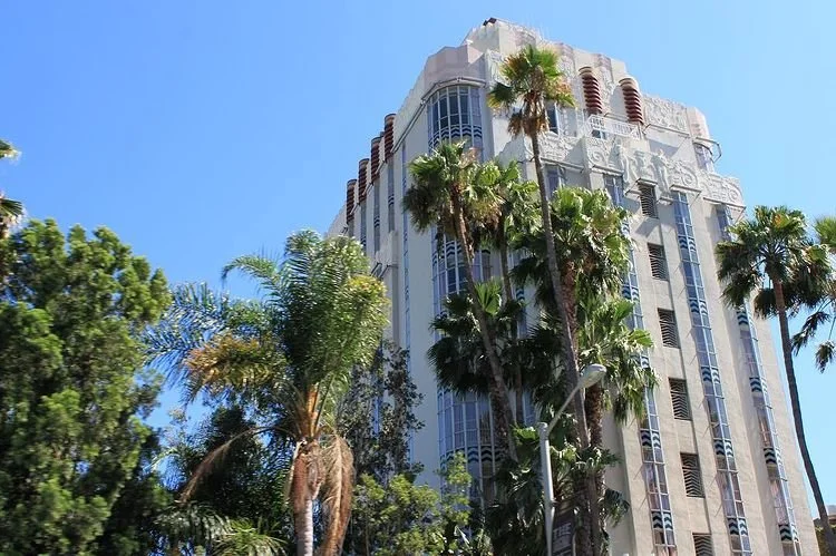A tall building with art deco architecture surrounded by palm trees under a clear blue sky.