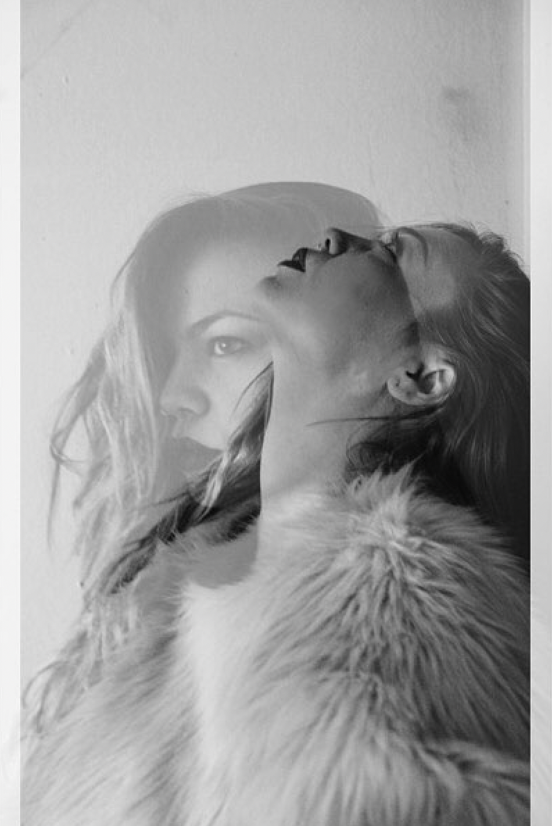 A black and white double exposure photograph of a woman with long hair and a fur coat, and a dog with long hair, both with closed eyes, creating an overlapping artistic portrait.