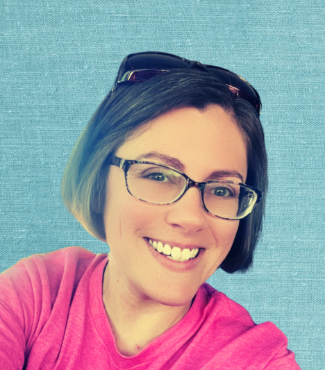 A woman with short dark hair, wearing glasses and a pink shirt, smiling in front of a blue background.