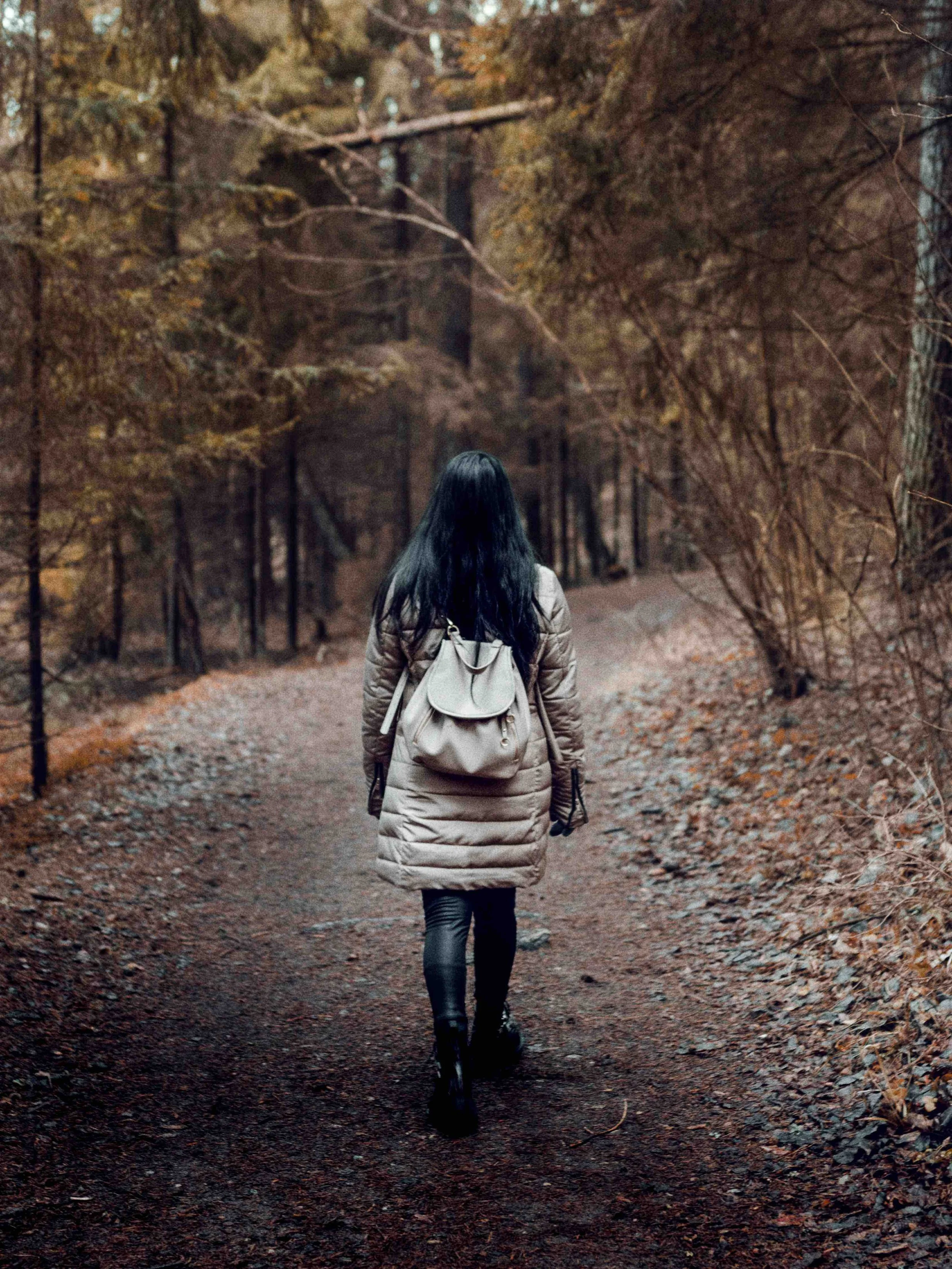 Girl with black hair in jacket walking on path in the woods towards anxiety therapy to release her trauma in somatic therapy