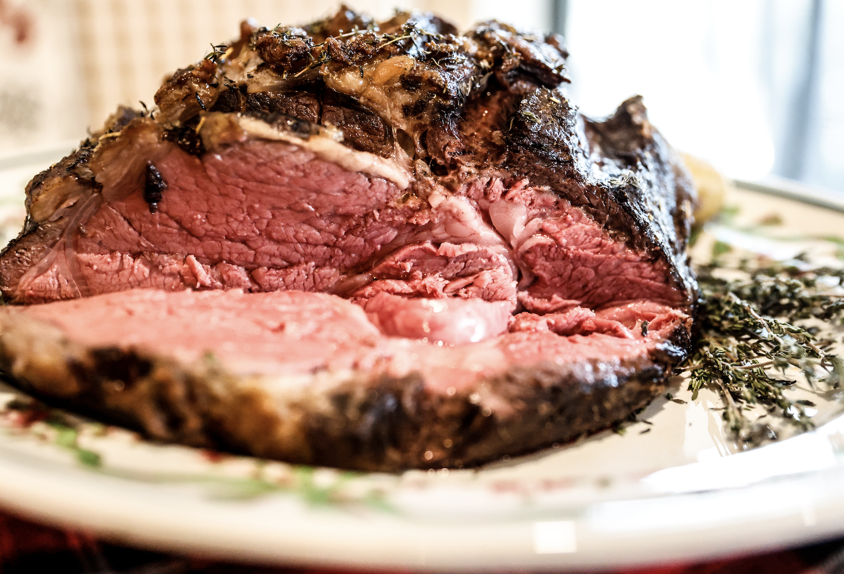 Cooked bison steak with a pink interior on a decorated serving platter with herbs.